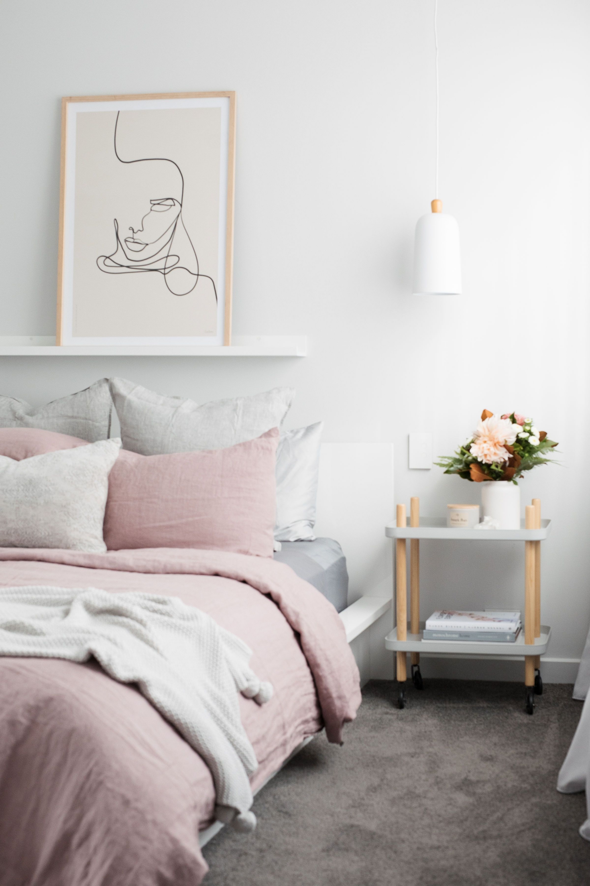 Phòng ngủ với 3 gam màu trắng - hồng - xám được thiết kế theo phong cách tối giản, phụ kiện trang trí chỉ đơn giản là bức tranh trừu tượng và lọ hoa duyên dáng, táp đầu giường đồng thời là chiếc kệ có lắp bánh xe nên cực kỳ linh hoạt.