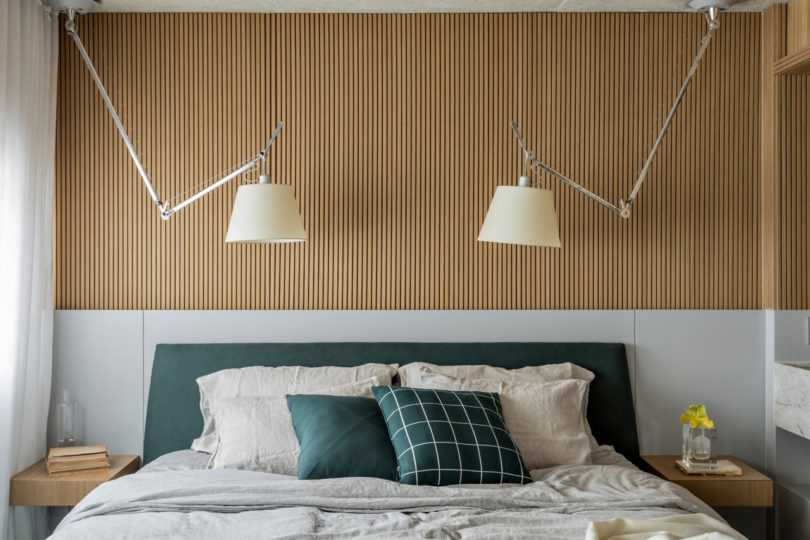 Bức tường khu vực phòng ngủ kết hợp gỗ tự nhiên sáng màu và gam màu trắng, cùng với sắc xanh cho cảm giác rất gần gũi. Cặp đèn ngủ đối xứng cũng tạo nên điểm nhấn cho phòng ngủ thanh lịch này.