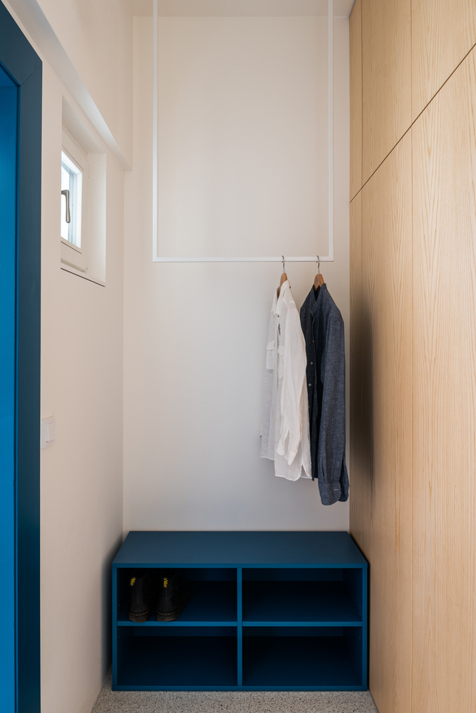 Lối vào của căn hộ tuy hẹp nhưng vẫn được tận dụng để bố trí thanh treo quần áo và một kệ  mở đựng giày dép 4 ngăn rộng rãi. Màu sơn xanh lam của kệ nổi bật trên nền tường trắng và “tone sur tone” với cửa ra vào.