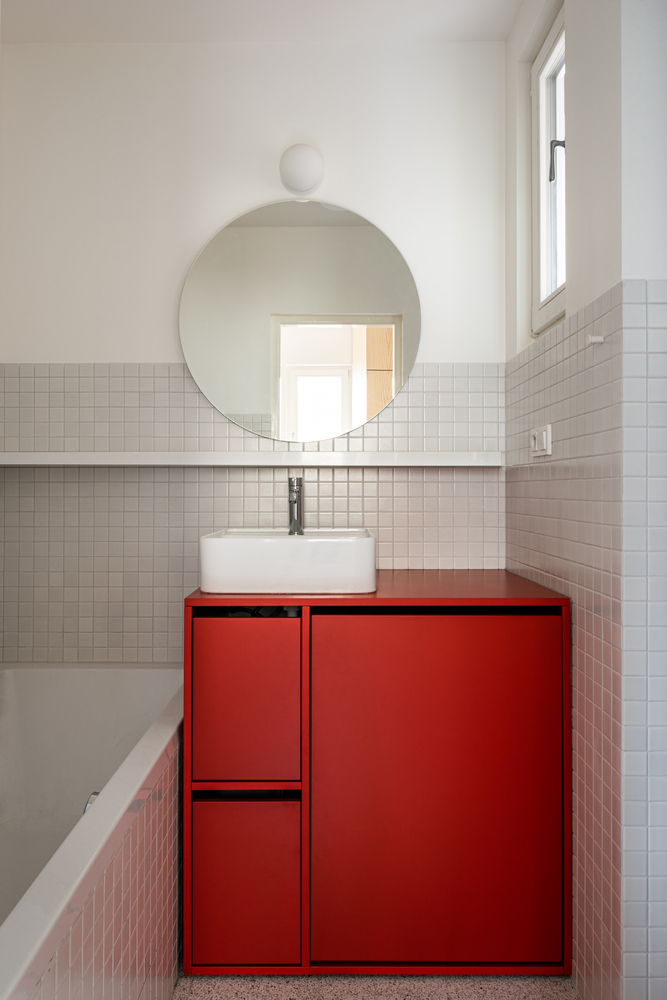 Bồn rửa tay bố trí trên chiếc tủ lưu trữ với sắc đỏ rực rỡ tương tự như ở quầy bar của phòng bếp. Tấm gương tròn giản dị trên tường, bố trí gần cửa sổ nhỏ để tận dụng ánh sáng tự nhiên, góp phần “cơi nới” không gian cho phòng tắm.