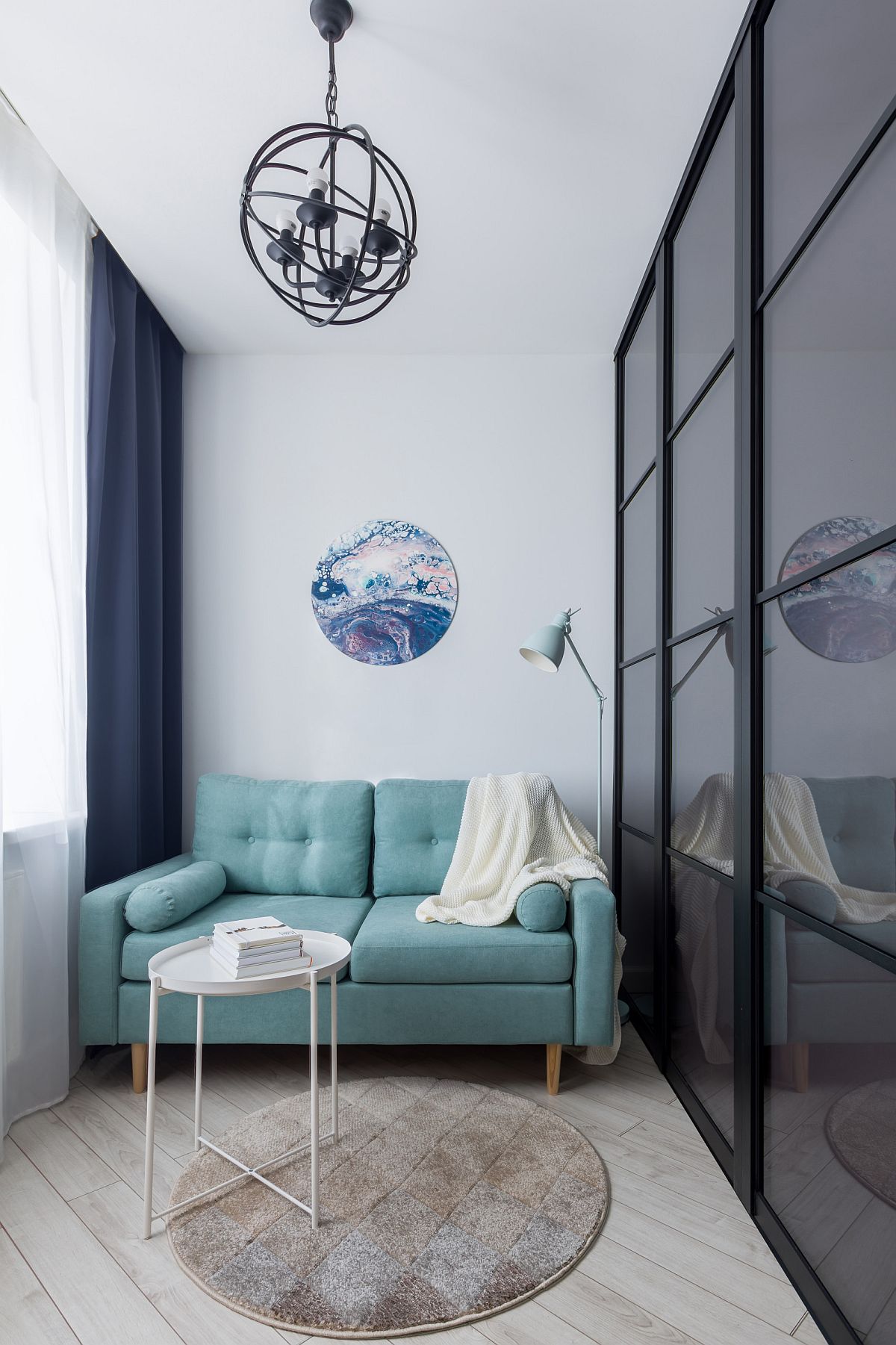 Chiếc ghế sofa màu xanh dương nhạt trong khu vực tiếp khách của căn hộ kiểu studio siêu nhỏ. Sự lựa chọn gam màu dịu nhẹ cùng thảm trải sàn và bức tranh thủy mặc hình tròn mang đến cảm giác bình yên và thư thái vô cùng. 