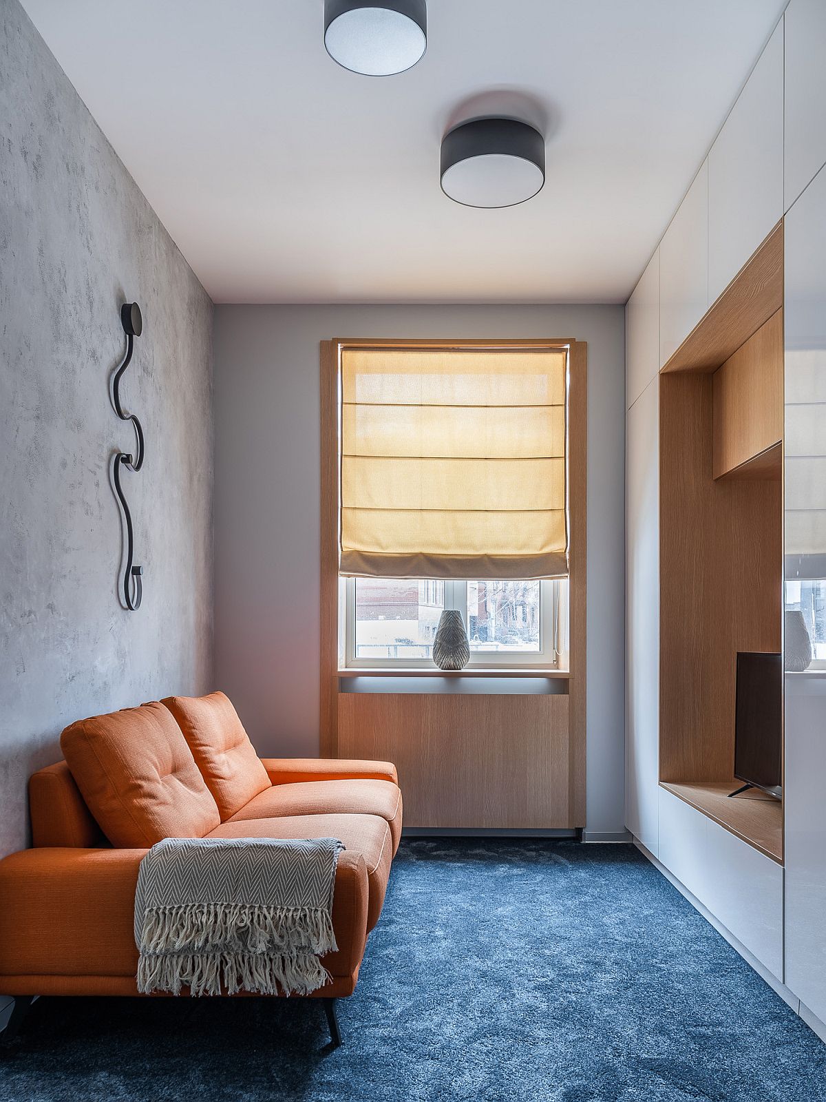 Loại bỏ chiếc bàn nước, phòng khách nhỏ nhắn này chỉ sử dụng duy nhất chiếc sofa da màu cam gạch nổi bật trên nền thảm xanh dương đậm và bức tường xám cho cái nhìn vừa rực rỡ vừa trung tính. 
