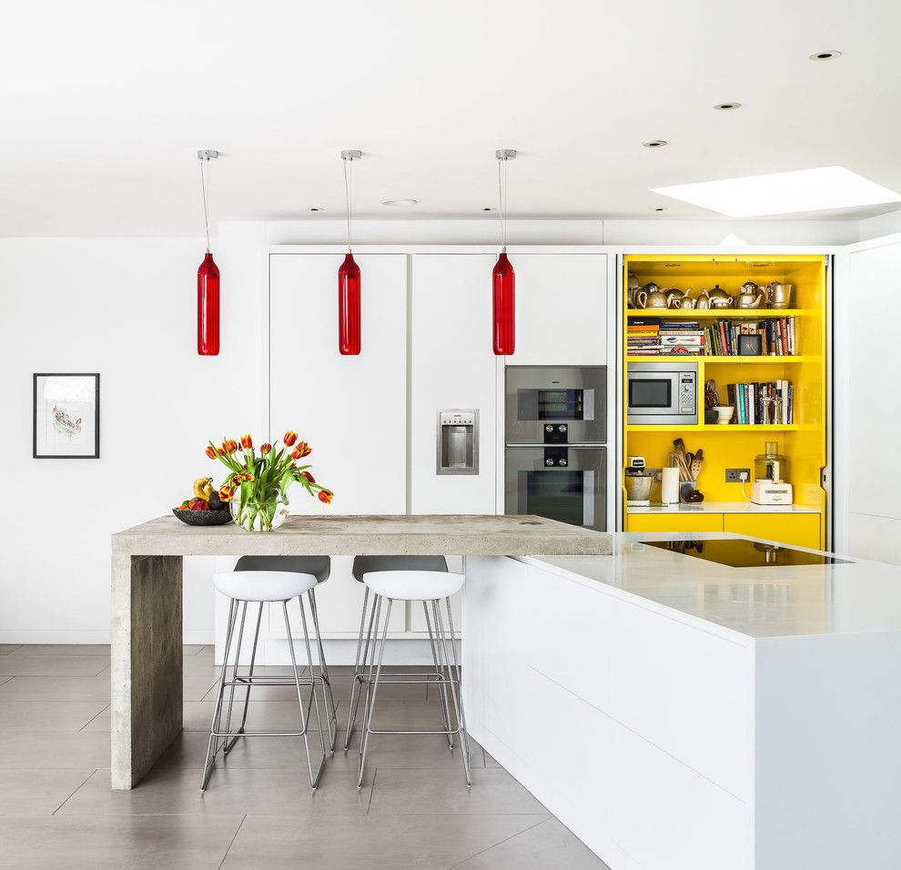 Phòng bếp phong cách hiện đại với những điểm nhấn nổi bật từ sắc màu. Chiếc bàn ăn mặt bê tông sần nhám tạo nên cái nhìn gần gũi cạnh đảo bếp màu trắng sáng bóng.