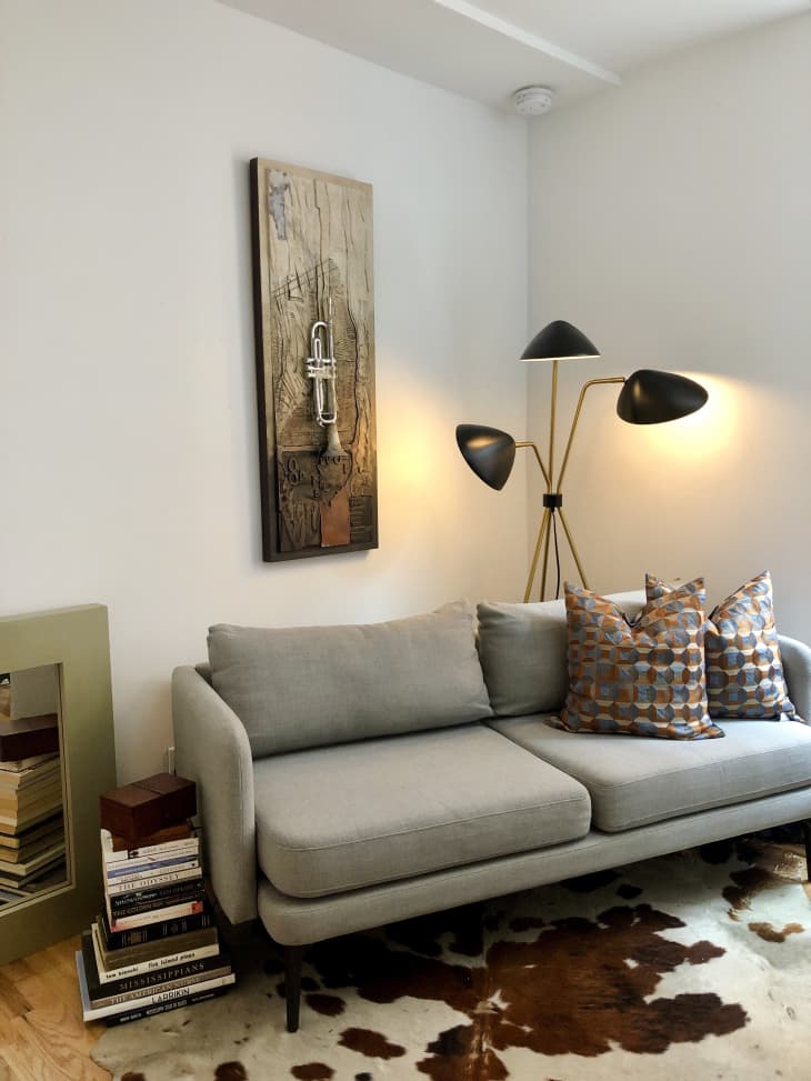 Phòng khách nhỏ xinh với sofa giản dị, thảm lông ấm áp, chiếc đèn và tranh treo tường và 'chiếc bàn phụ' làm từ chồng sách ấn tượng.