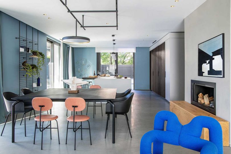 Bố cục chính của biệt thự là một không gian mở với phòng bếp, phòng ăn và phòng khách liên kết cùng nhau với những bức tường màu xanh lam. Bộ bàn ăn màu đen huyền bí và màu cam gạch xen kẽ, cùng với đèn thả trần bắt mắt.
