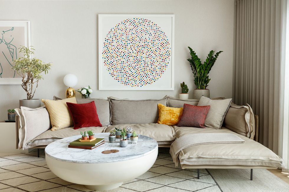 Phòng khách đầy ấm áp và mời gọi với ghế sofa góc êm ái cùng gối tựa nhiều màu sắc, bức tranh treo tường khiến ta liên tưởng đến hình ảnh sinh động của kính vạn hoa.