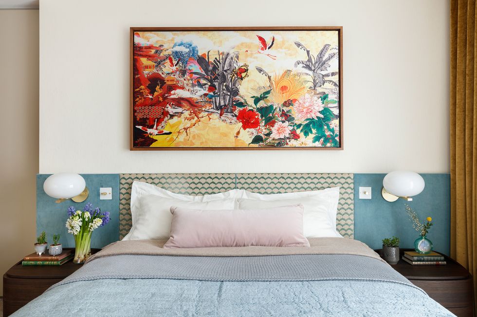 Phòng ngủ của bố mẹ thiết kế sống động với sự kết hợp của rất nhiều màu sắc. Một bức tranh hoa nổi bật trên nền tường trắng. Khu vực đầu giường trang trí bằng hoa văn như vẩy cá xếp lớp cùng những sắc xanh dịu nhẹ tạo cảm giác như đang ở giữa đại dương bao la.