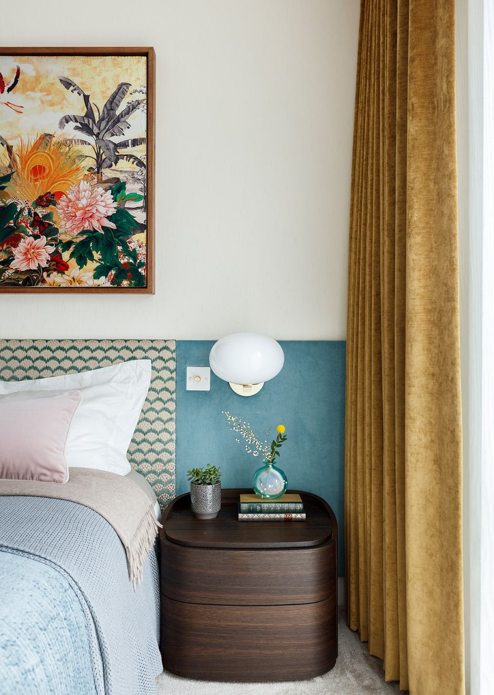 Táp đầu giường bằng gỗ đậm màu, đơn giản nhưng sang trọng và tiện ích. Bên trên đặt một lọ hoa thủy tinh, sách và chậu cây sen đá. Chiếc đèn ngủ hình tròn gắn tường đối xứng trông rất thanh lịch.