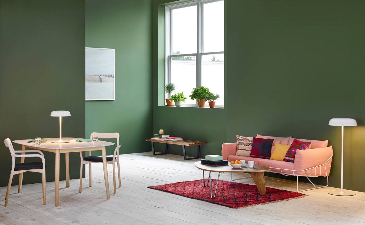 Bức tường màu xanh rêu đậm trở nên cực kỳ ấn tượng khi sánh đôi cùng gam màu hồng san hô của chiếc ghế sofa, tấm thảm đỏ và những chiếc gối tựa đủ sắc màu.