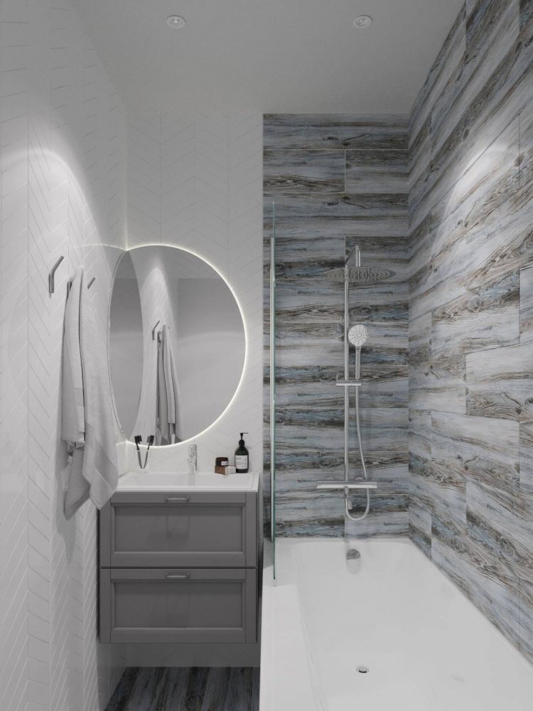 Phòng tắm sang trọng với gam màu xám trắng. Bồn tắm nằm được phân vùng với bồn rửa tích hợp tủ lưu trữ bằng vách ngăn kính trong suốt. Tấm gương lớn và sự chuyển tiếp vật liệu ốp tường giữa hai khu vực cũng tạo nên điểm nhấn cho phòng tắm nhỏ xinh này.