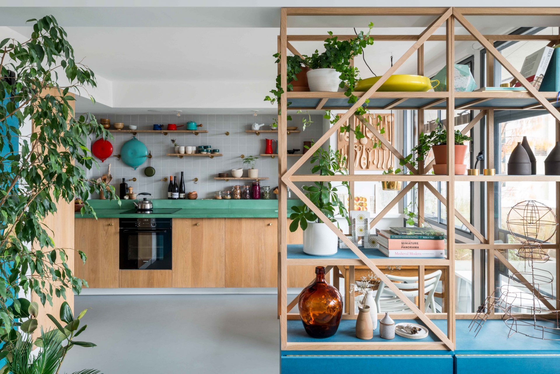 Tầng dưới của căn hộ là không gian dành cho phòng bếp và khu vực tiếp khách. Bếp được thiết kế kiểu chữ I với tủ gỗ sồi mà mặt bàn bê tông sơn màu xanh ngọc lục bảo. 
