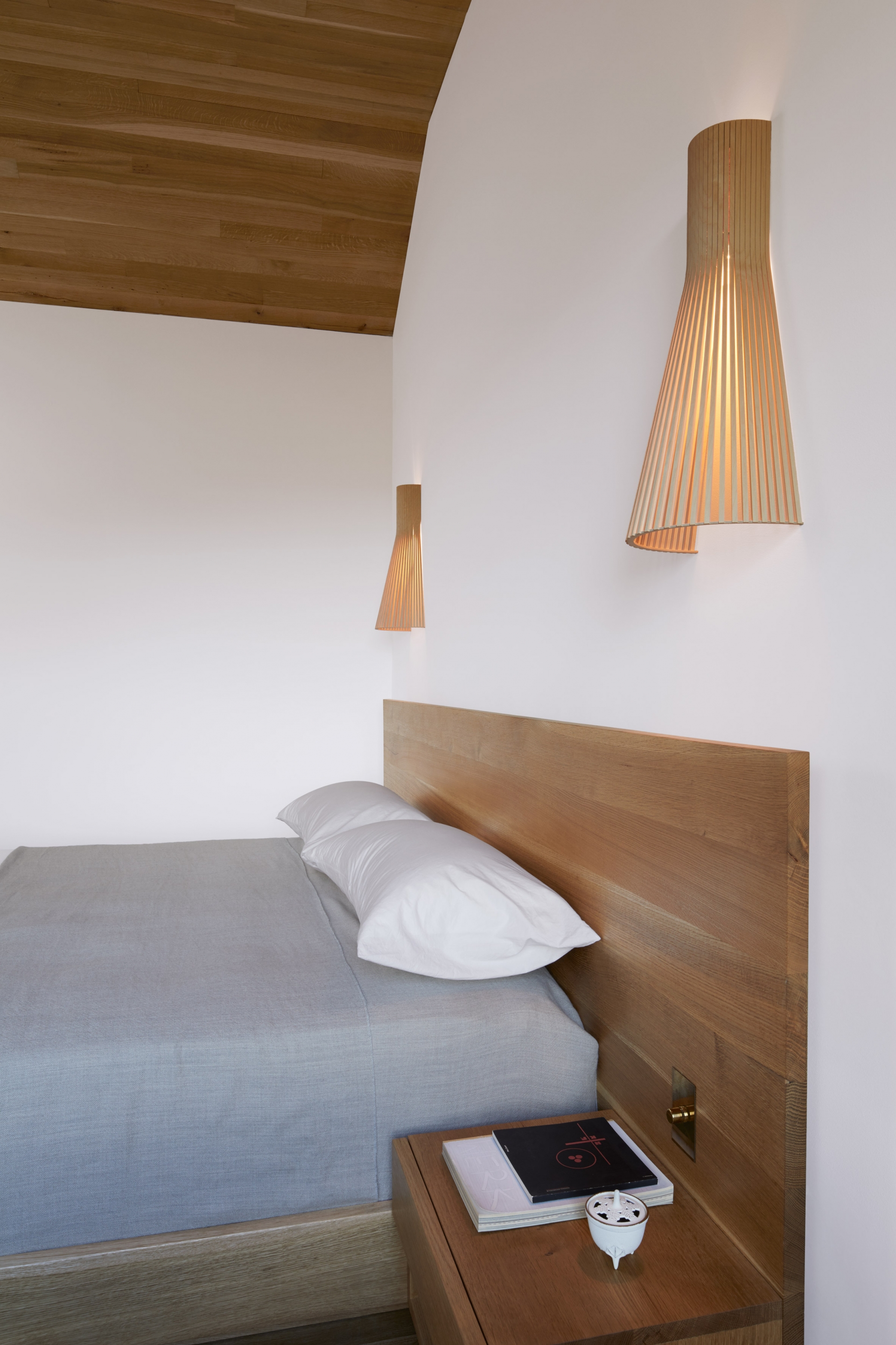 Phòng ngủ của bố mẹ được thiết kế tối giản với khung giường gỗ, ga bọc giường màu xám nhẹ nhàng cùng cặp đèn ngủ bằng tre kiểu dáng cổ điển.