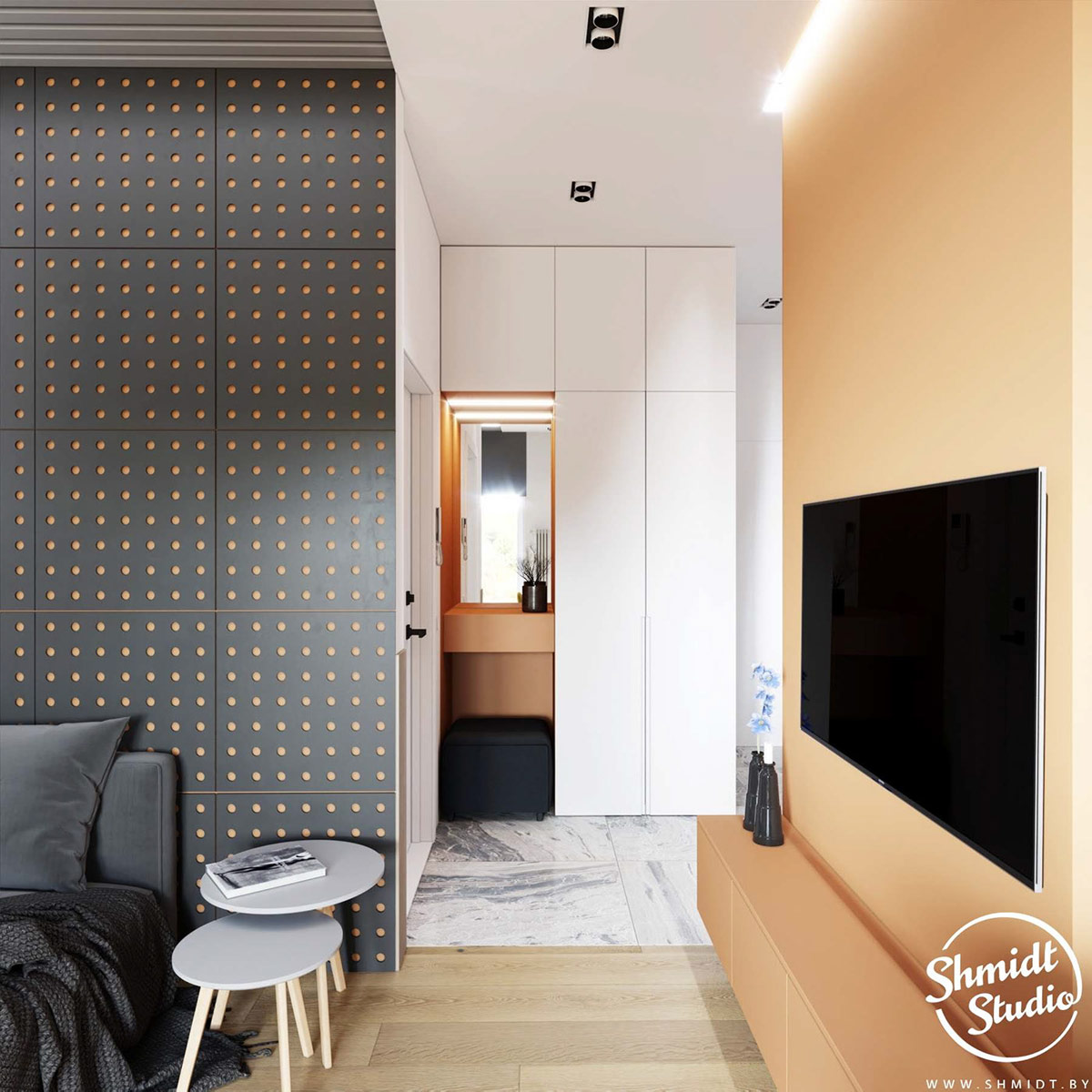 Bức tường treo tivi được sơn màu cam tươi sáng. Từ góc nhìn này bạn sẽ thấy sự liên kết màu sắc từ góc nhỏ ở lối vào căn hộ - nơi bố trí gương soi và ghế nghỉ - cũng sơn màu tương tự. Bảng Pegboard màu đen tạo sự tương phản và chiều sâu cho phòng khách.