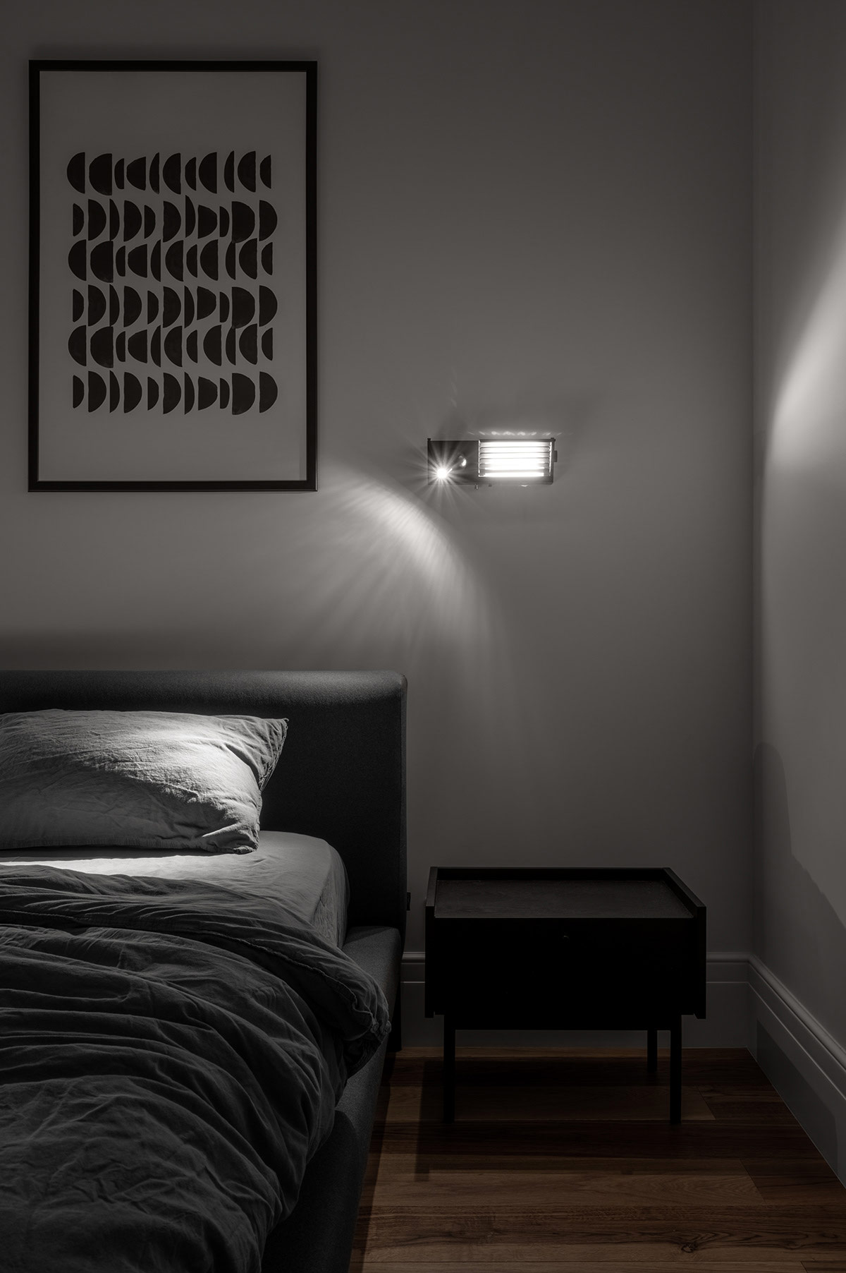 Chiếc táp đầu giường màu đen vân gỗ tự nhiên bố trí đối xứng hai bên tạo sự tương phản nhẹ nhàng với sàn nhà lát gỗ sồi màu nâu mộc mạc. Khi đêm về, chiếc đèn ngủ hiện đại giúp căn phòng trở nên đẹp mắt hơn, nó có thể điều chỉnh ánh sáng để chủ nhân đọc sách.