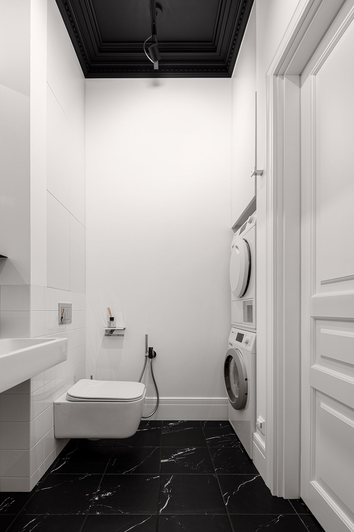 Phòng tắm của căn hộ tuy nhỏ nhưng cực kỳ bắt mắt nhờ cách sử dụng màu sắc đối lập giữa nền tường và nội thất màu trắng với trần và sàn nhà màu đen. Sàn nhà lát đá cẩm thạch, vật liệu sang trọng và đắt giá với những đường vân trắng hài hòa với ý đồ thiết kế.