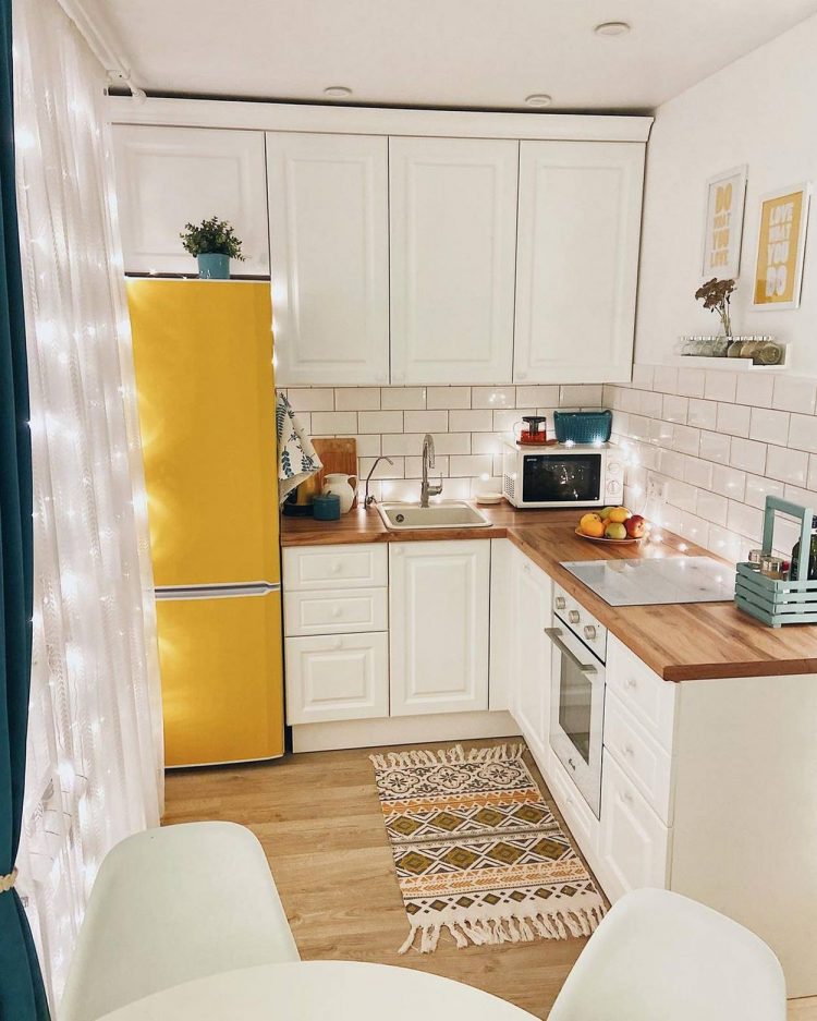 Phòng bếp lựa chọn thiết kế chữ L siêu nhỏ nhưng siêu xinh với chiếc tủ lạnh màu vàng mù tạt cực kỳ nổi bật, phía trên còn đặt 1 chậu hoa dễ thương. Hệ tủ bếp trên và dưới đồng bộ màu trắng, mặt bàn bếp ốp gỗ tối màu tạo sự tương phản ấn tượng.
