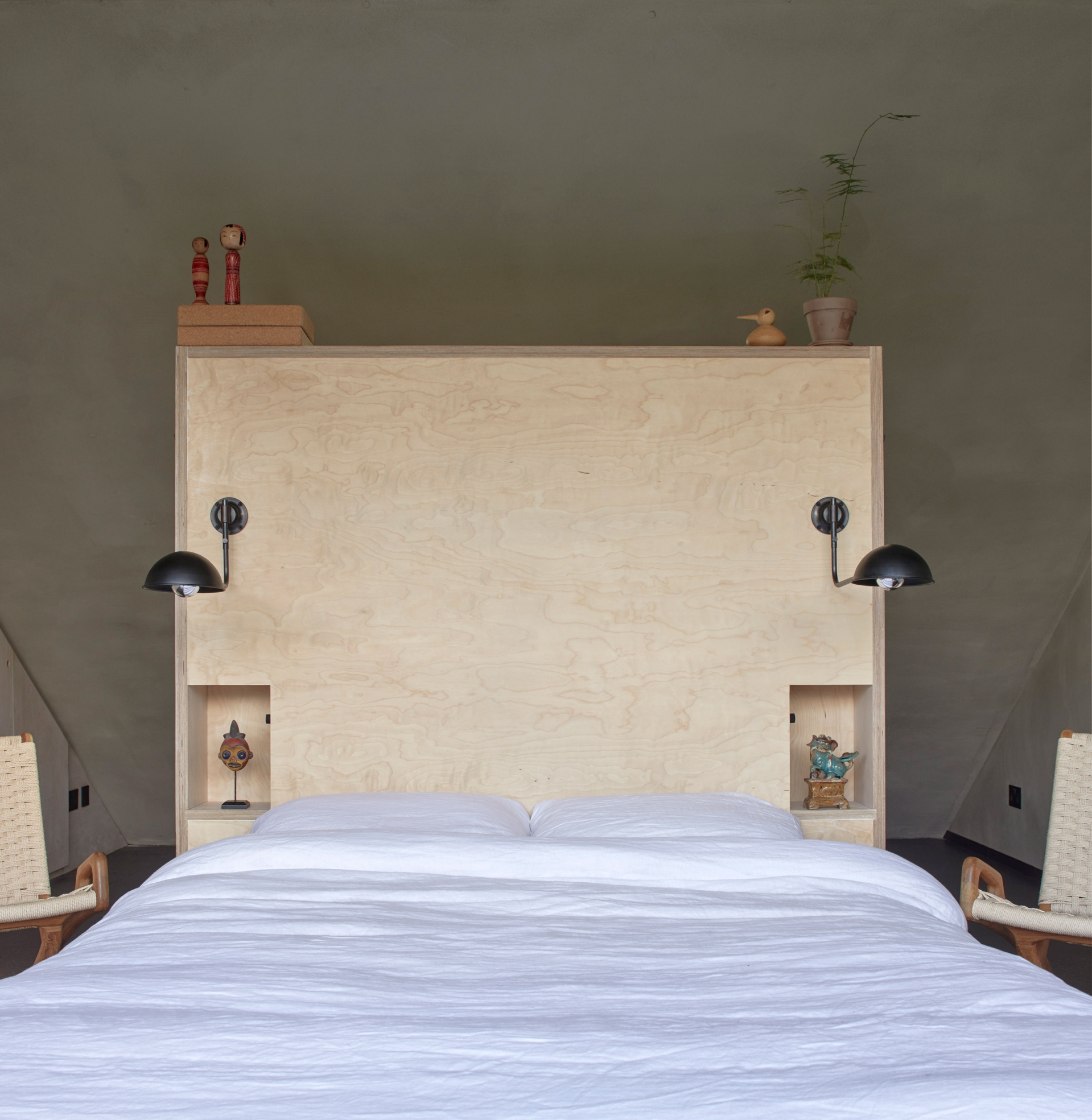 Phần đầu giường được bố trí ở phần mái dốc, có thiết kế đơn giản bằng gỗ sáng màu, đệm và chăn ga gối đồng nhất một màu trắng nhẹ nhàng, sạch sẽ.