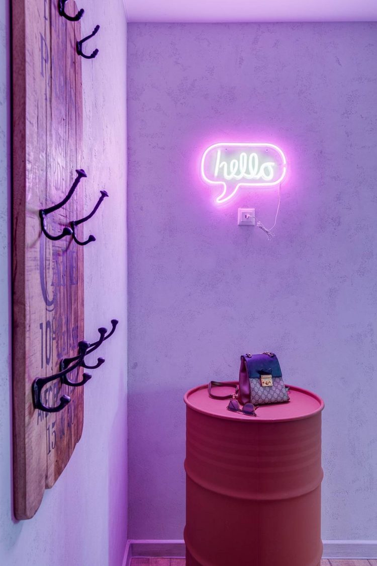 Những chiếc móc kim loại nhỏ sơn màu đen gắn trên tấm bảng gỗ để treo áo khoác, mũ nón, chìa khóa,... một cách gọn gàng. Chiếc thùng phuy bằng kim loại phủ sơn màu hồng để cất đồ đạc, kết hợp đèn LED với dòng chữ “hello” lấp lánh đầy mời gọi.