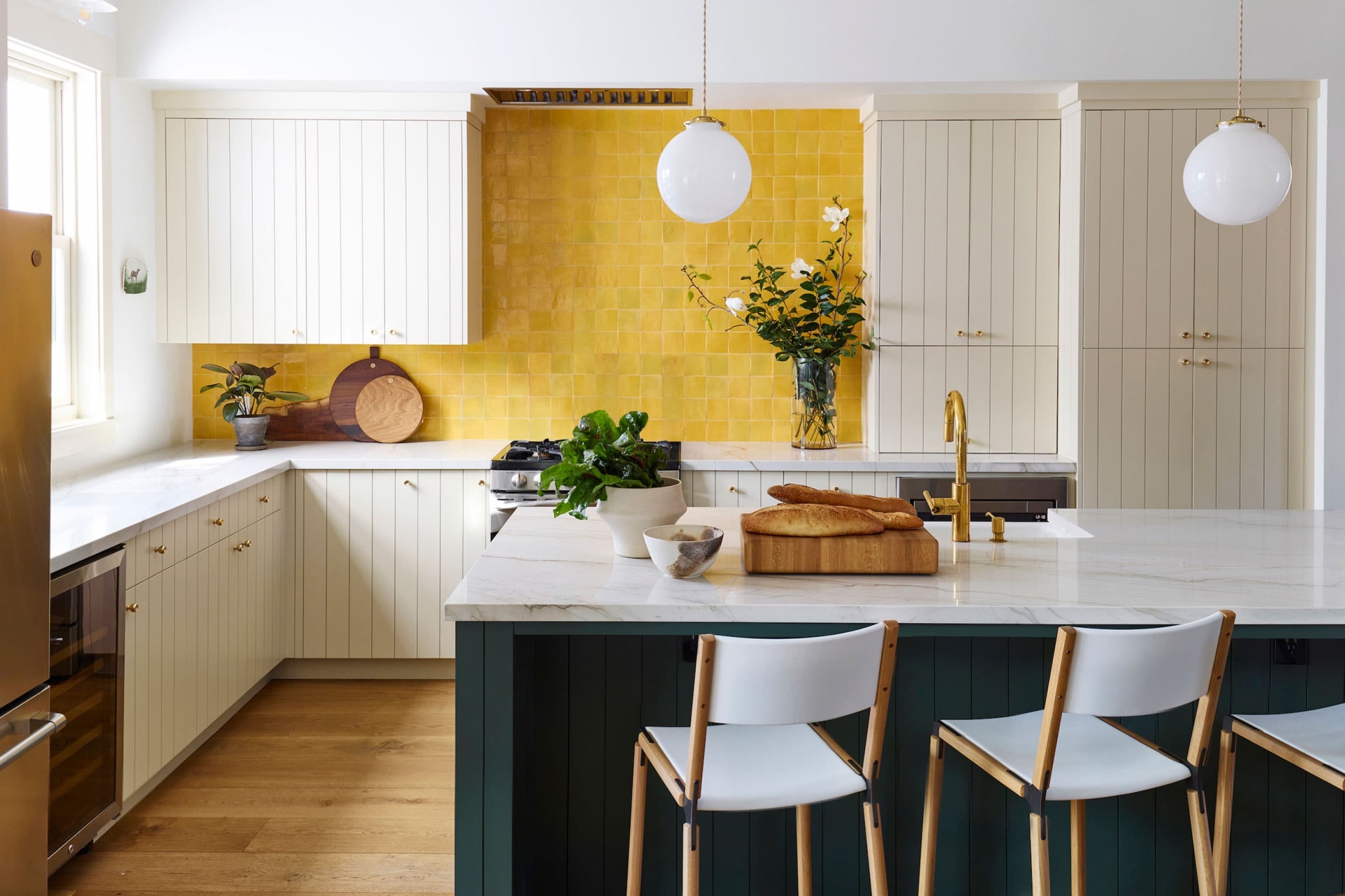 Phòng bếp với sự phối màu đẹp như một bức tranh vẽ với gam màu trắng chủ đạo cho hệ tủ bếp, mặt bàn, đảo bếp màu xanh lá cây đậm, cùng với đó là khu vực backsplash ốp những viên đá hình vuông màu vàng nhỏ nhắn, sáng rực cả góc phòng.