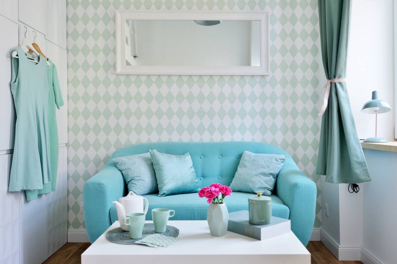 Phòng khách với chiếc ghế sofa màu ngọc lam êm ái, đằng sau bức tường là tấm gương dài hình chữ nhật để “nhân đôi” căn phòng bằng thị giác. Trên chiếc bàn nước màu trắng, các phụ kiện trang trí được lựa chọn “tone sur tone” xinh đẹp vô cùng.