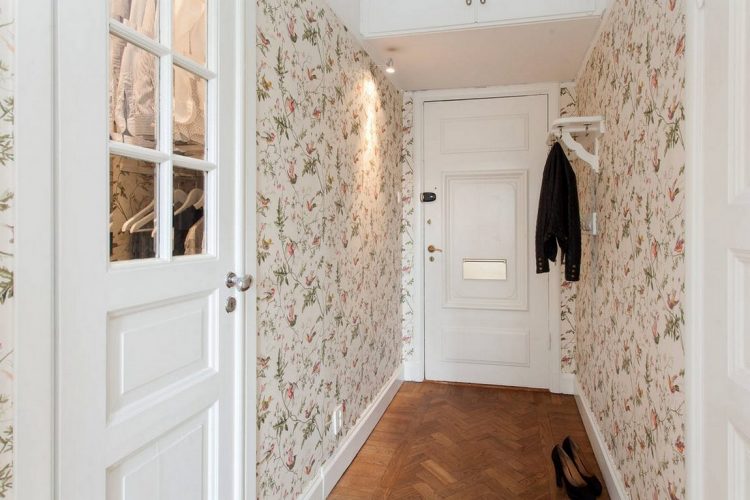 Lối vào căn hộ 38m² với cánh cửa sơn trắng nhẹ nhàng, xung quanh là những bức tường khóa lên mình tấm giấy dán hoa lá chim muông mang đậm phong cách vintage.