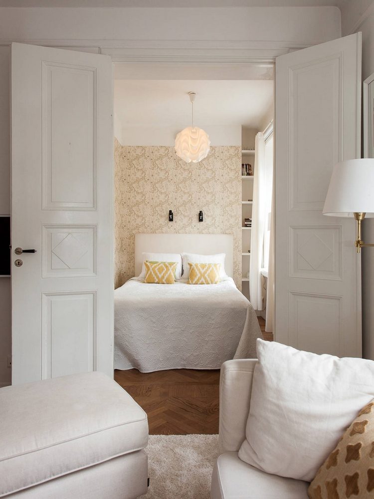 Góc phải phòng khách là phòng ngủ được thiết kế sau cánh cửa một cách riêng tư, kín đáo. Chiếc đèn trần trong căn phòng như một bông hoa trắng dịu dàng xinh đẹp.