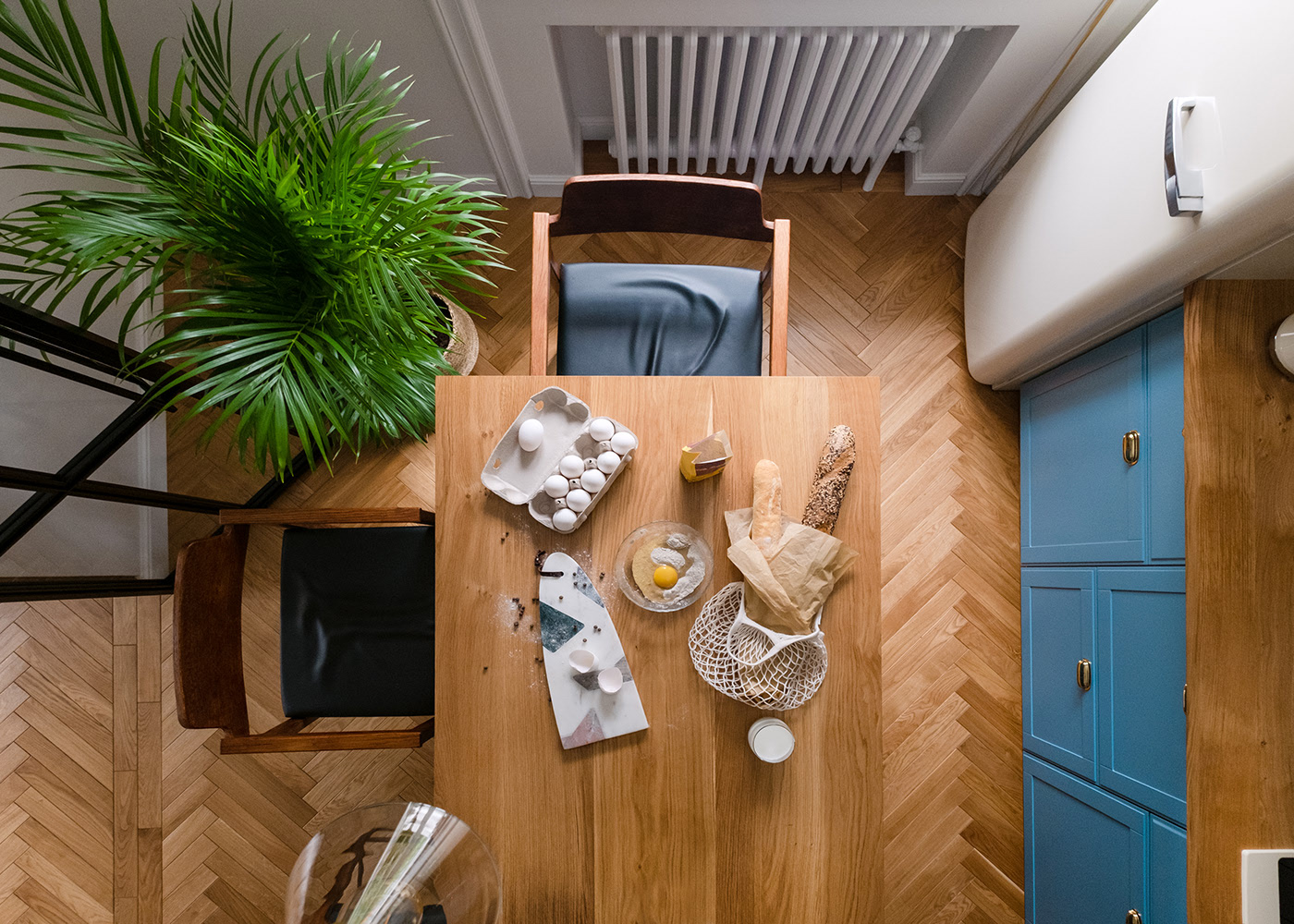 Phòng bếp chụp từ trên cao cho thấy sự hòa quyện giữa sàn gỗ họa tiết xương cá hiện đại với mặt bàn bằng gỗ, chậu cây cảnh tô điểm cho không gian thêm tươi mát.