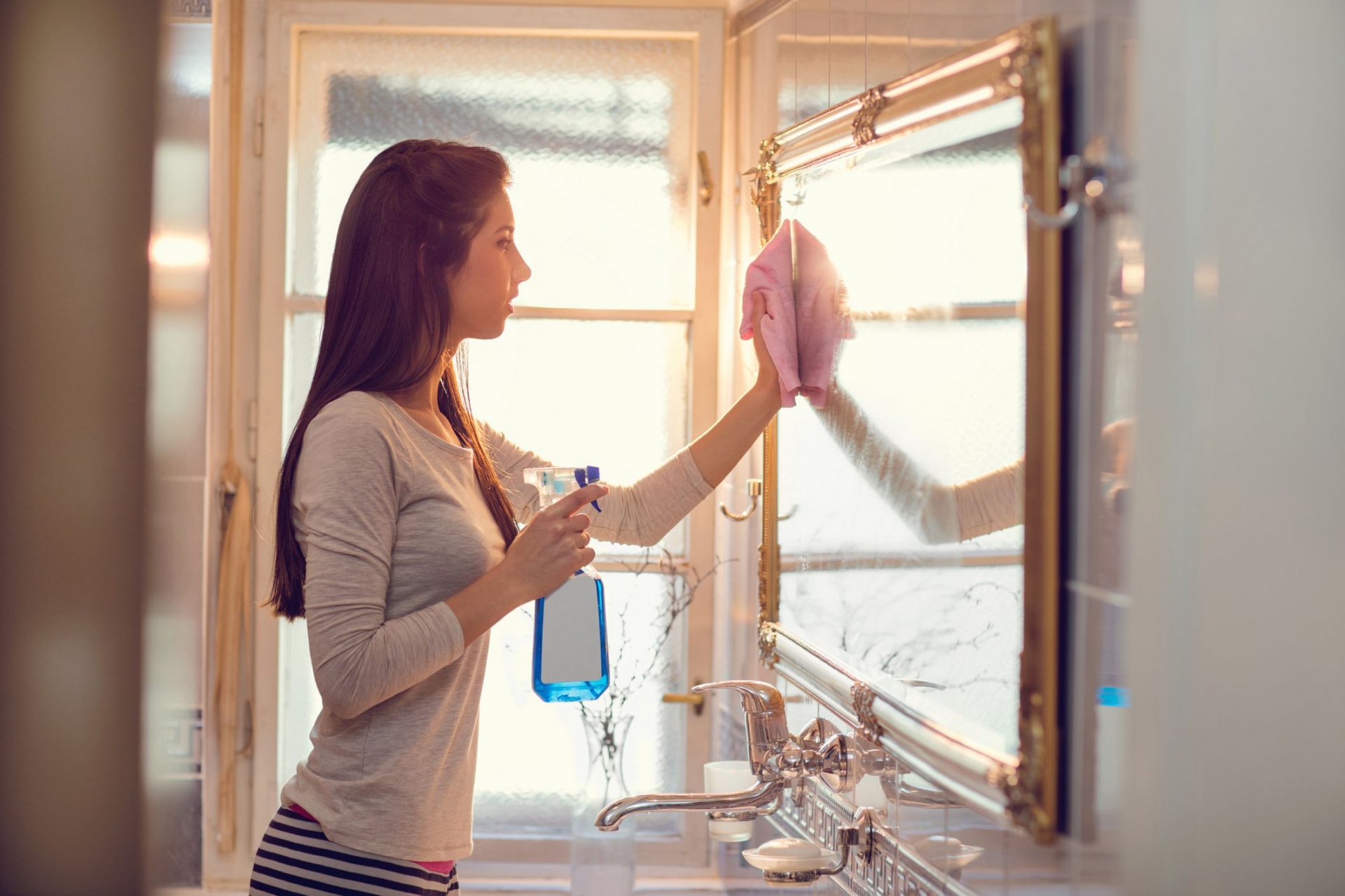 Dùng nước lau kính chuyên dụng xịt lên gương soi và các bề mặt cửa kính trong phòng tắm.