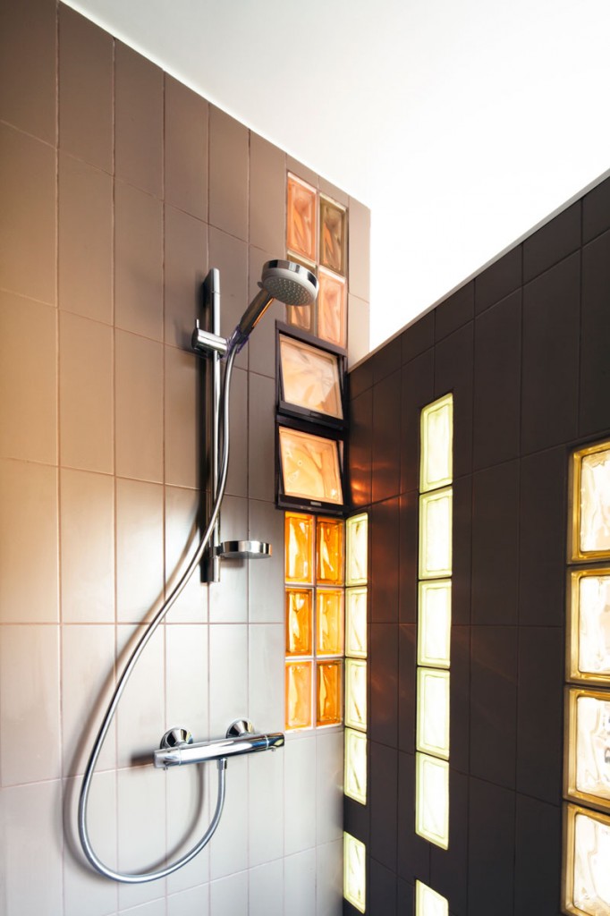 Phòng tắm siêu nhỏ với vòi tắm hoa sen, những viên gạch màu cam nổi bật giữa phông nền màu đen huyền bí, đồng thời gợi nhớ về bức tường ở khu vực tiếp khách, tạo nên sự liên kết trong tổng thể.