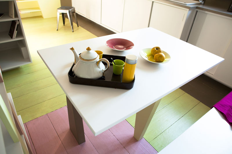 Sàn phòng khách được sơn nhiều màu sắc khác nhau, chiếc bàn nước (đồng thời là bàn ăn) với mặt bàn màu trắng đã trở thành phông nền hoàn hảo để các vật dụng như ấm trà, ly tách, bát đĩa,... đặt trên nó trở nên thu hút.