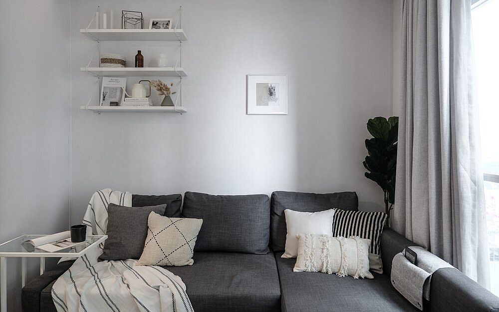 Sofa phòng khách kiểu module đặt sát trong bức tường cạnh ô cửa đầy nắng ấm. Chiếc bàn phụ mặt kính trong suốt ở góc trái và một chiếc túi đựng điện thoại cực kỳ sáng tạo tận dụng phần tay vịn bên phải sofa.