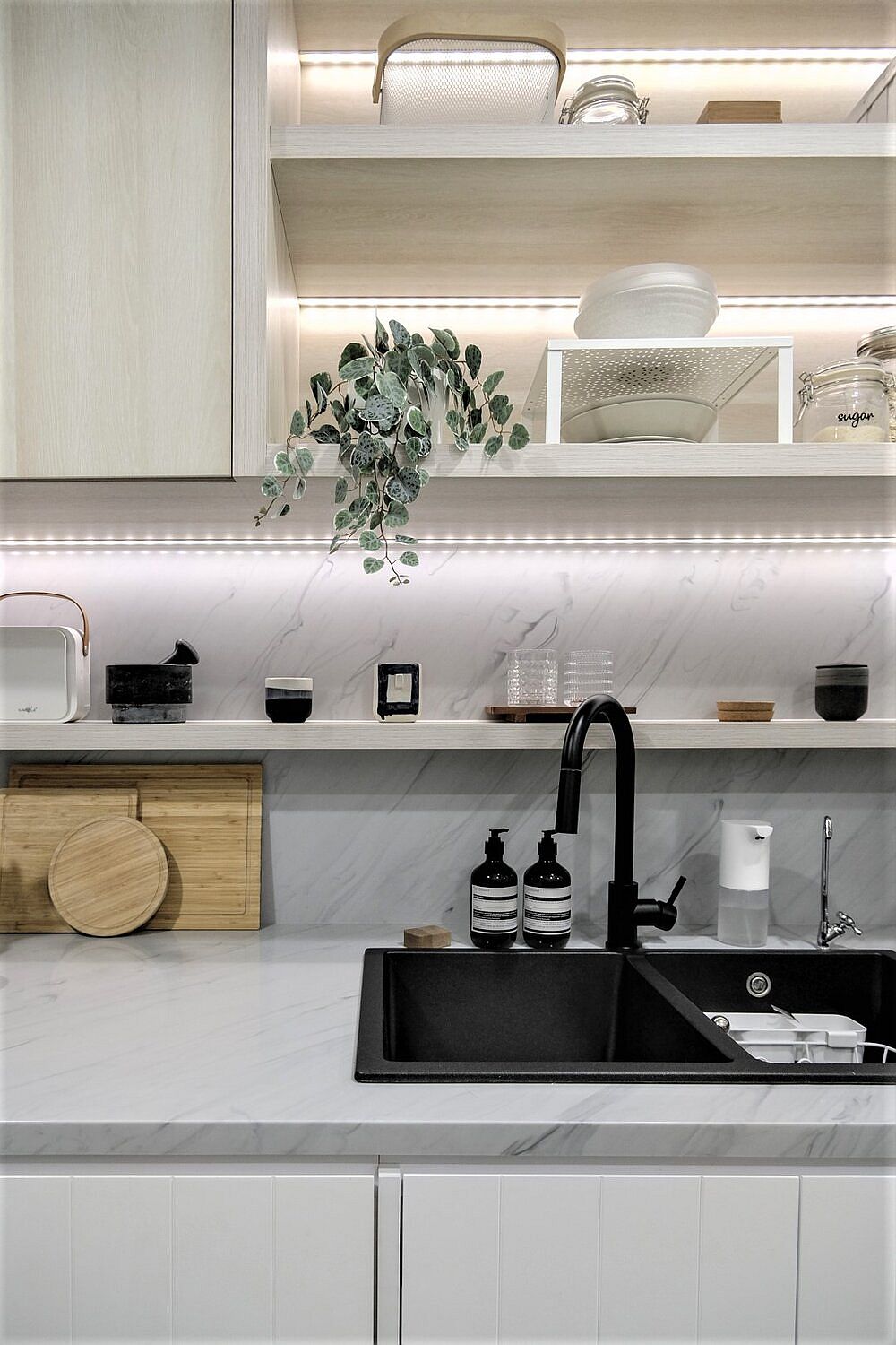 Bồn rửa màu đen cho cảm giác vững chắc và sạch sẽ. Dải đèn LED xinh xắn được bố trí chạy ngang dưới các kệ bếp vừa cung cấp ánh sáng vừa tạo sự lấp lánh bắt mắt giữa những gam màu trung tính được lựa chọn làm sắc màu chủ đạo.