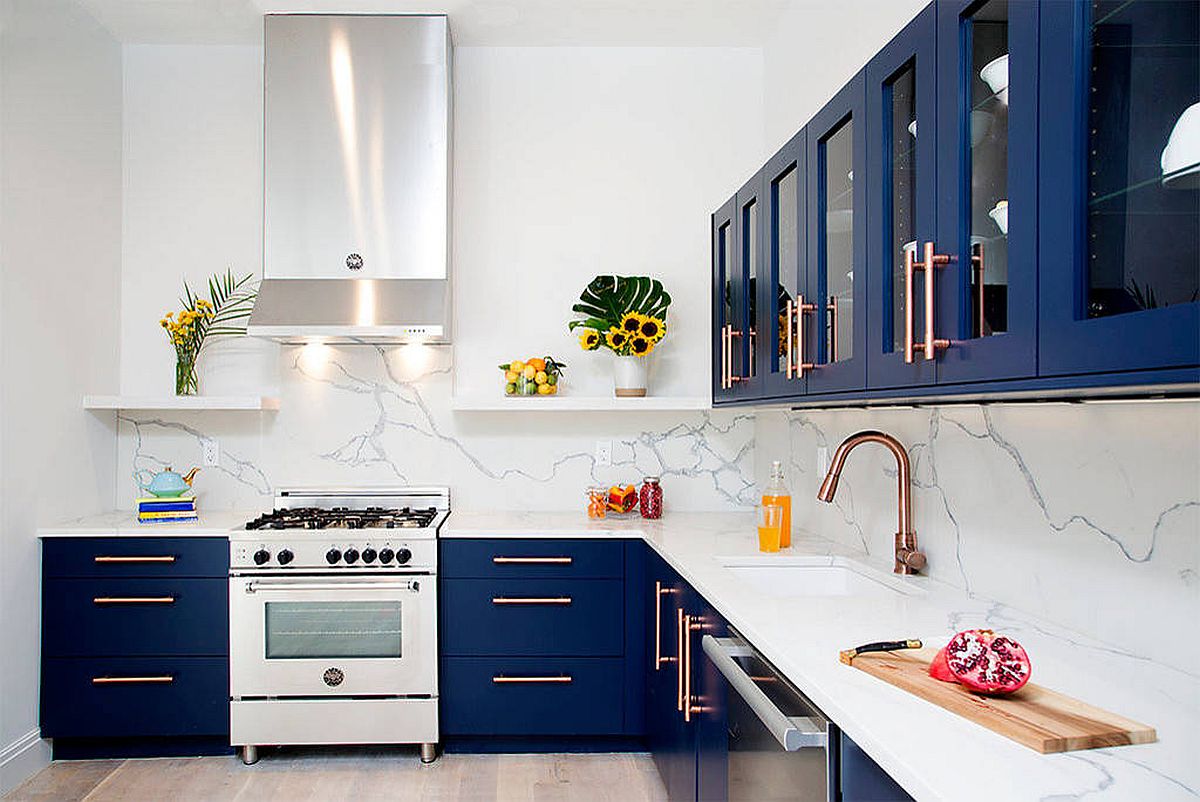 Phòng bếp có thiết kế chữ I hiện đại với tủ màu xanh lam, tấm ốp lát đá cẩm thạch trắng và những điểm nhấn bằng đồng ở vòi rửa và tay nắm cửa tủ.