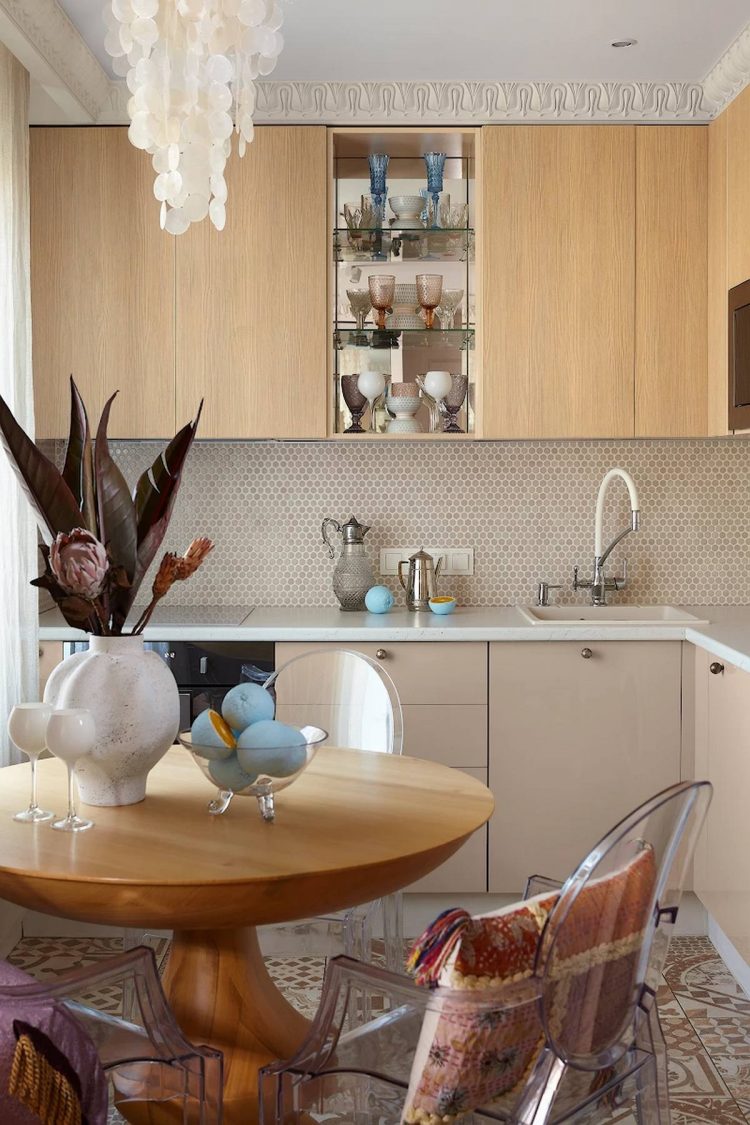Phòng bếp thiết kế kiểu chữ L phù hợp với cấu trúc nhỏ của căn hộ. Một phần kệ mở trong suốt ở giữa tủ gỗ trên tạo vẻ đẹp mềm mại. Màu gỗ tự nhiên cùng màu sơn ngọc trai ở tủ dưới cũng tạo nên tương quan sắc màu trong tổng thể.
