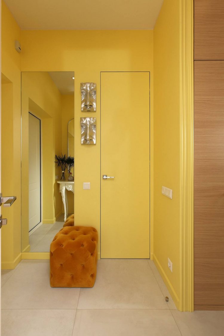 Lối vào ấn tượng với toàn bộ bức tường sơn vàng vàng tươi sáng. Tấm gương dọc kích thước bằng với cánh cửa là giải pháp cực kỳ thông minh, vừa giúp nhân đôi không gian vừa không khiến khu vực này bị chói lóa bởi sắc vàng bao phủ.