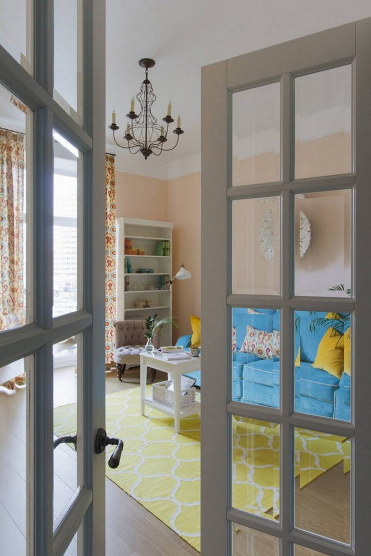 Phòng khách sau cánh cửa sơn xám thanh lịch, vừa nhìn từ bên ngoài đã thấy vô cùng nổi bật nhờ tấm thảm trải sàn màu vàng và ghế sofa màu ngọc lam tươi tắn.