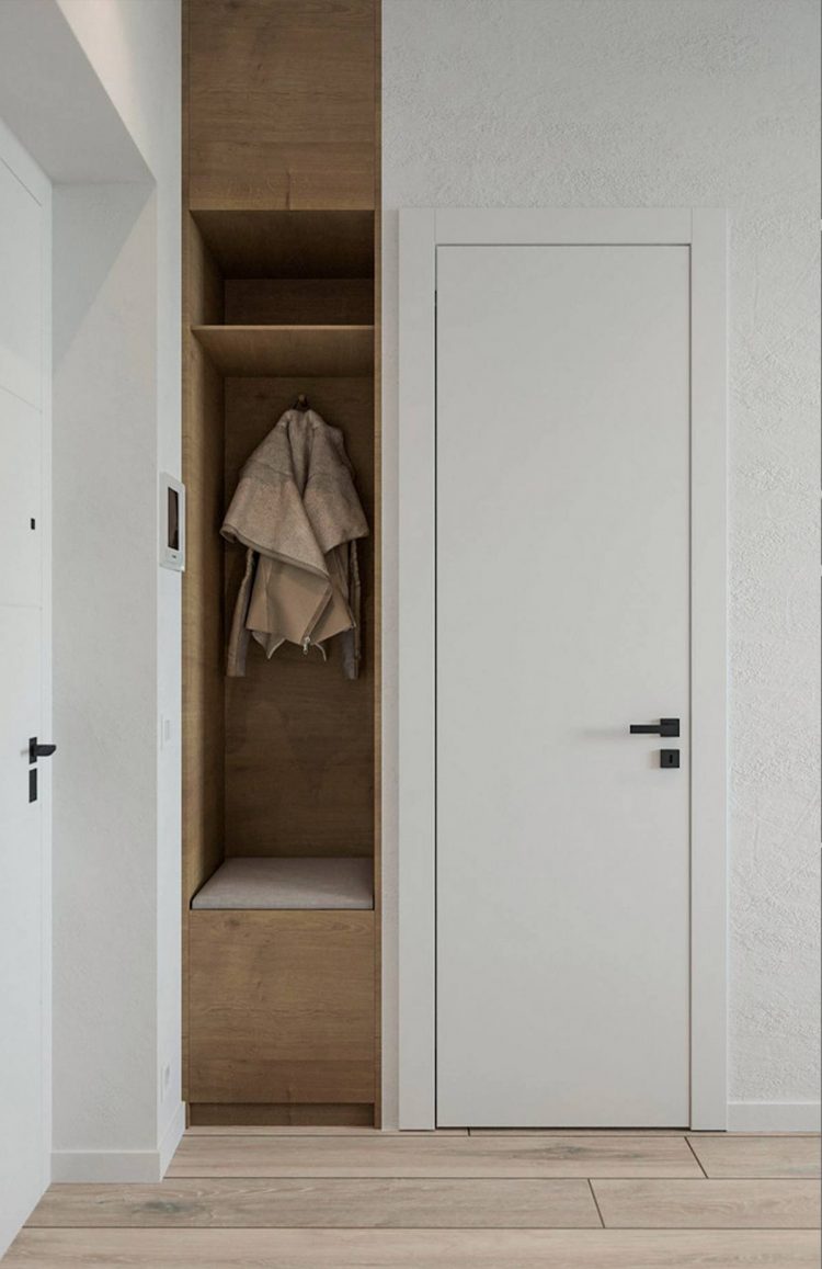 Lối vào căn hộ của cặp vợ chồng trẻ được thiết kế đơn giản với cánh cửa sơn trắng, hốc tường ốp gỗ được tận dụng làm góc treo áo khoác và ghế nghỉ chân thay giày.
