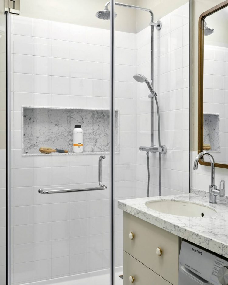 Để tiết kiệm diện tích, máy giặt được bố trí ngay bên dưới bồn rửa tay. Tấm gương lớn hình chữ nhật treo dọc bức tường để 'nhân đôi' không gian. Hốc tường tận dụng đặt sữa tắm, đồ vệ sinh cá nhân, phân vùng với toilet bằng cửa kính trong suốt.
