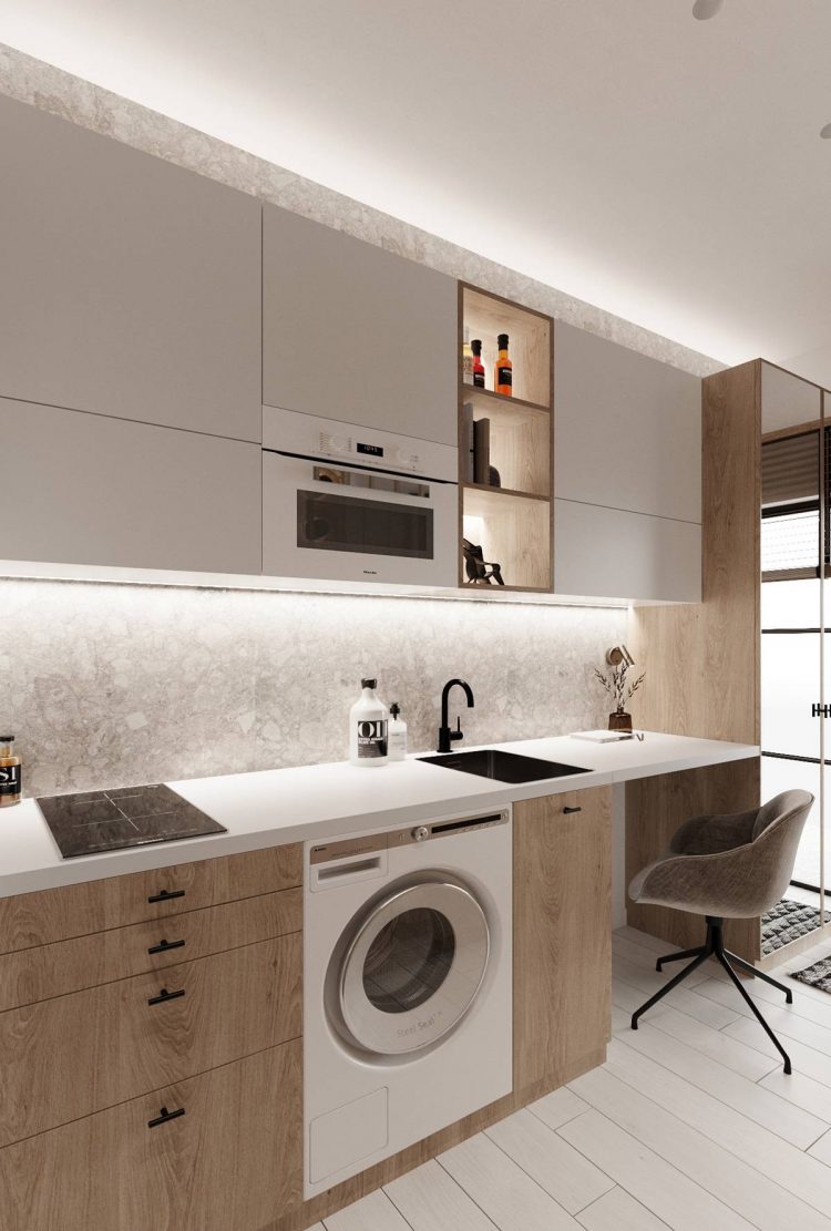 Thay vì bố trí trong phòng tắm, chiếc máy giặt màu trắng hiện đại được đặt ngay ở vị trí tủ bếp dưới. Khu vực bên cạnh bồn rửa màu đen là góc nhỏ dành cho chủ nhân căn hộ học tập hoặc làm việc.