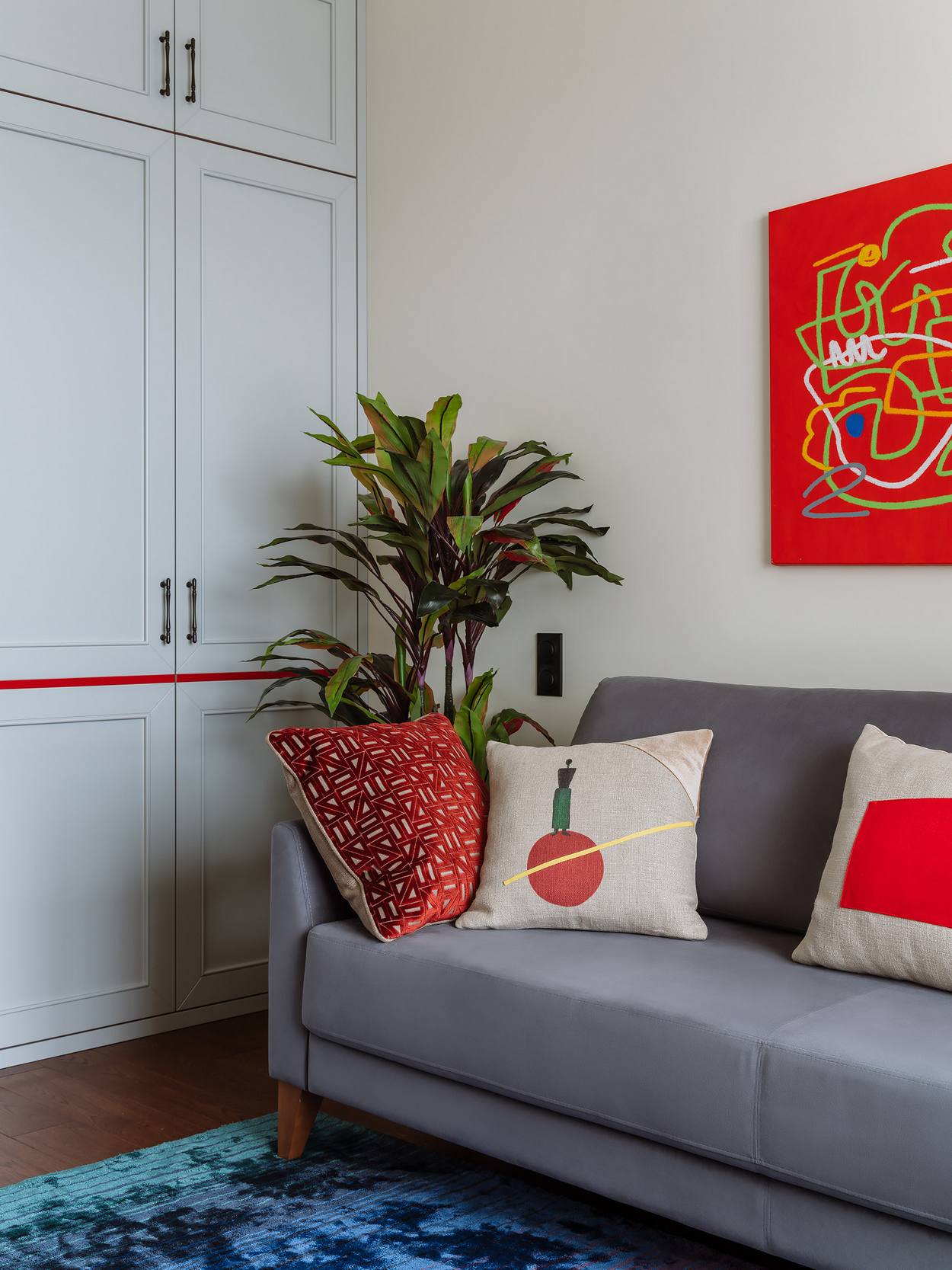 Những điểm nhấn màu đỏ được sử dụng một cách tiết chế nhằm mang đến sự quyến rũ cho không gian, từ những bức tranh trừu tượng trên tường, gối tựa họa tiết phong phú trên ghế sofa màu xám nhạt,...