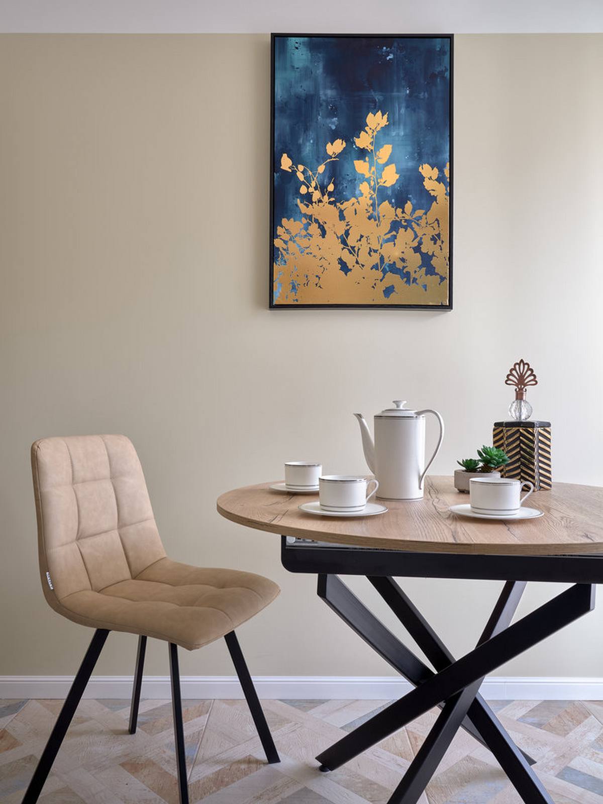Khu vực ăn uống được tích hợp trong phòng bếp, gồm chiếc bàn gỗ hình tròn và bộ ghế màu be. Cả bàn và ghế đều có phần chân màu đen cho cảm giác vững chãi. Bức tranh treo tường phối hợp giữa màu xanh lam đậm và vàng đồng tạo điểm nhấn quyến rũ trên bức tường.