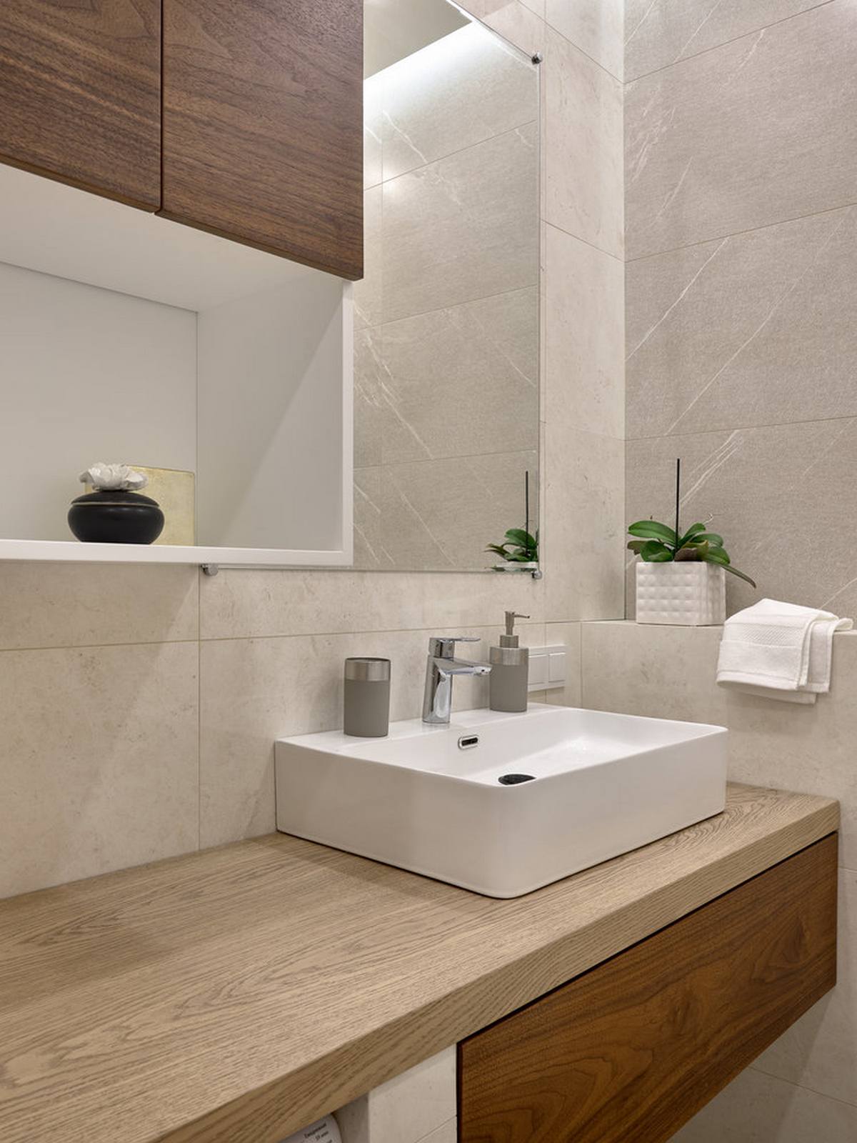 Khu vực phòng tắm sử dụng gạch ốp tường màu xám thanh lịch, tủ lưu trữ kết hợp bồn rửa tay bằng sứ bóng đẹp. Hệ thống kệ gắn tường cũng được tận dụng để tối ưu hóa không gian nhỏ.