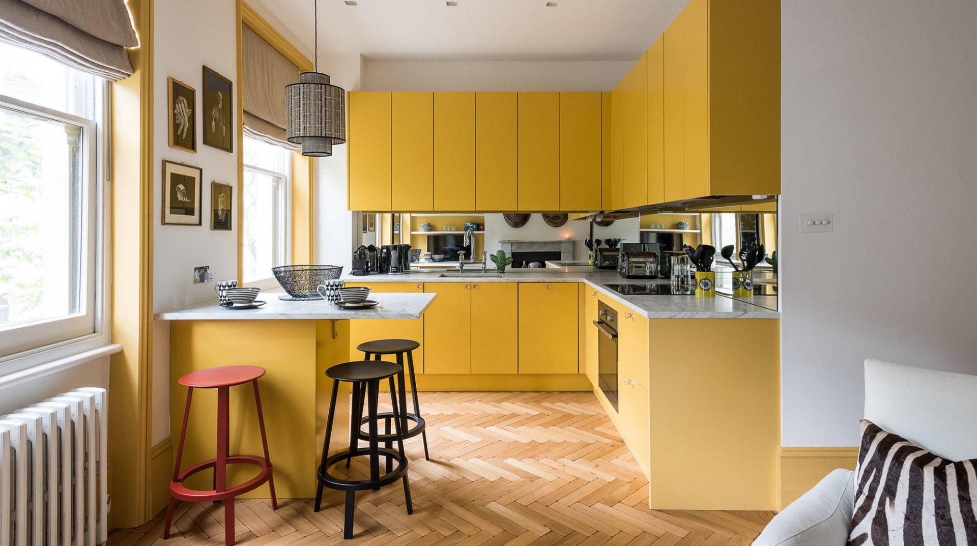 Phòng bếp có thiết kế kiểu chữ L sử dụng gam màu vàng cho cả hệ thống tủ bếp dưới và tủ bếp trên kịch trần cho không gian cao thoáng. Chiếc bàn ăn bố trí ở góc tường phối hợp ghế đẩu màu đỏ và đen tạo nên điểm nhấn đẹp mắt.