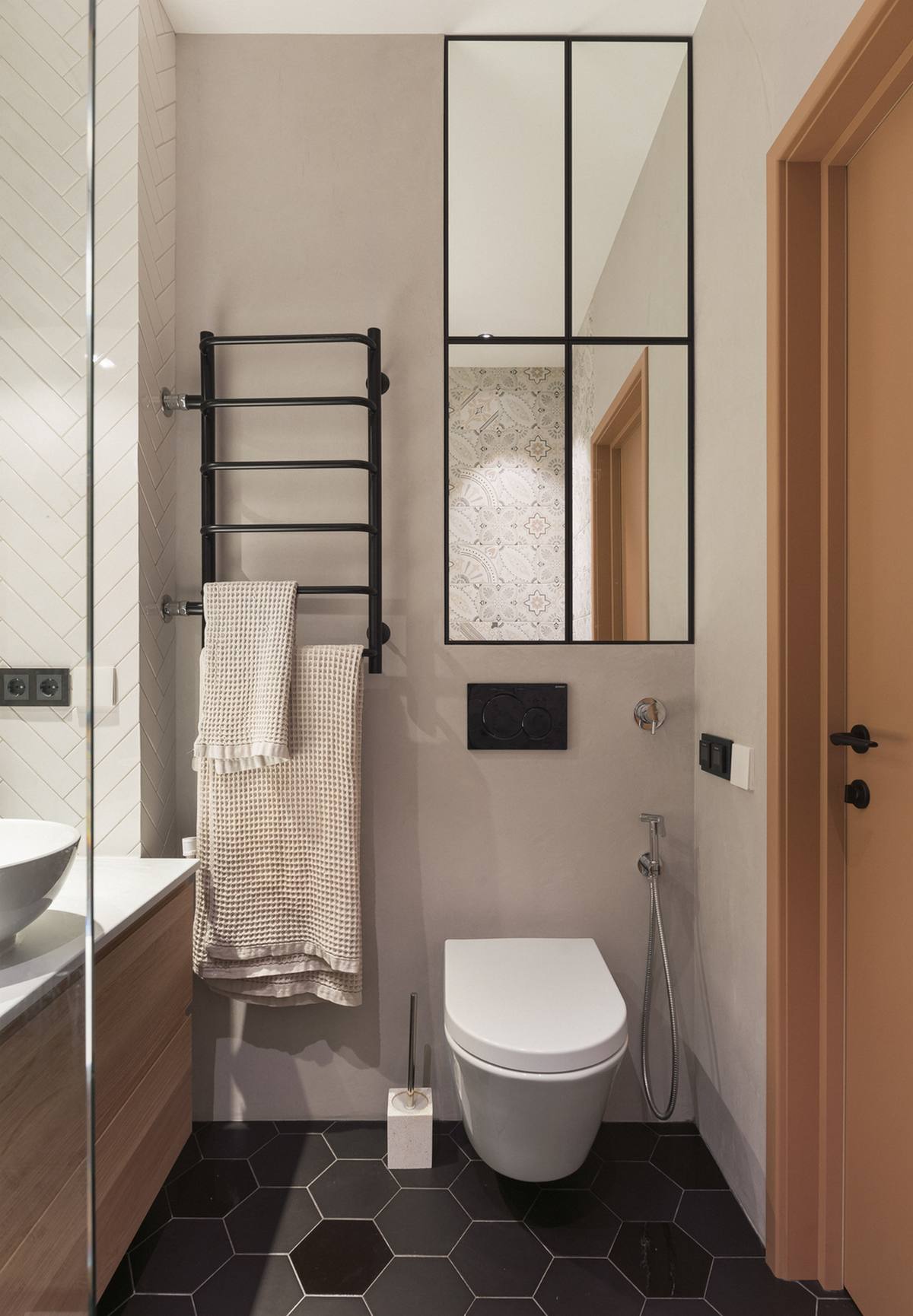 Phòng tắm nhỏ hẹp nên sử dụng bồn toilet treo tường để giải phóng diện tích sàn. Sàn nhà lát gạch tổ ong tối màu dễ dàng vệ sinh sạch sẽ. Chiếc tủ lưu trữ trên cao có bề mặt cửa ốp gương giúp 'cơi nới' không gian.