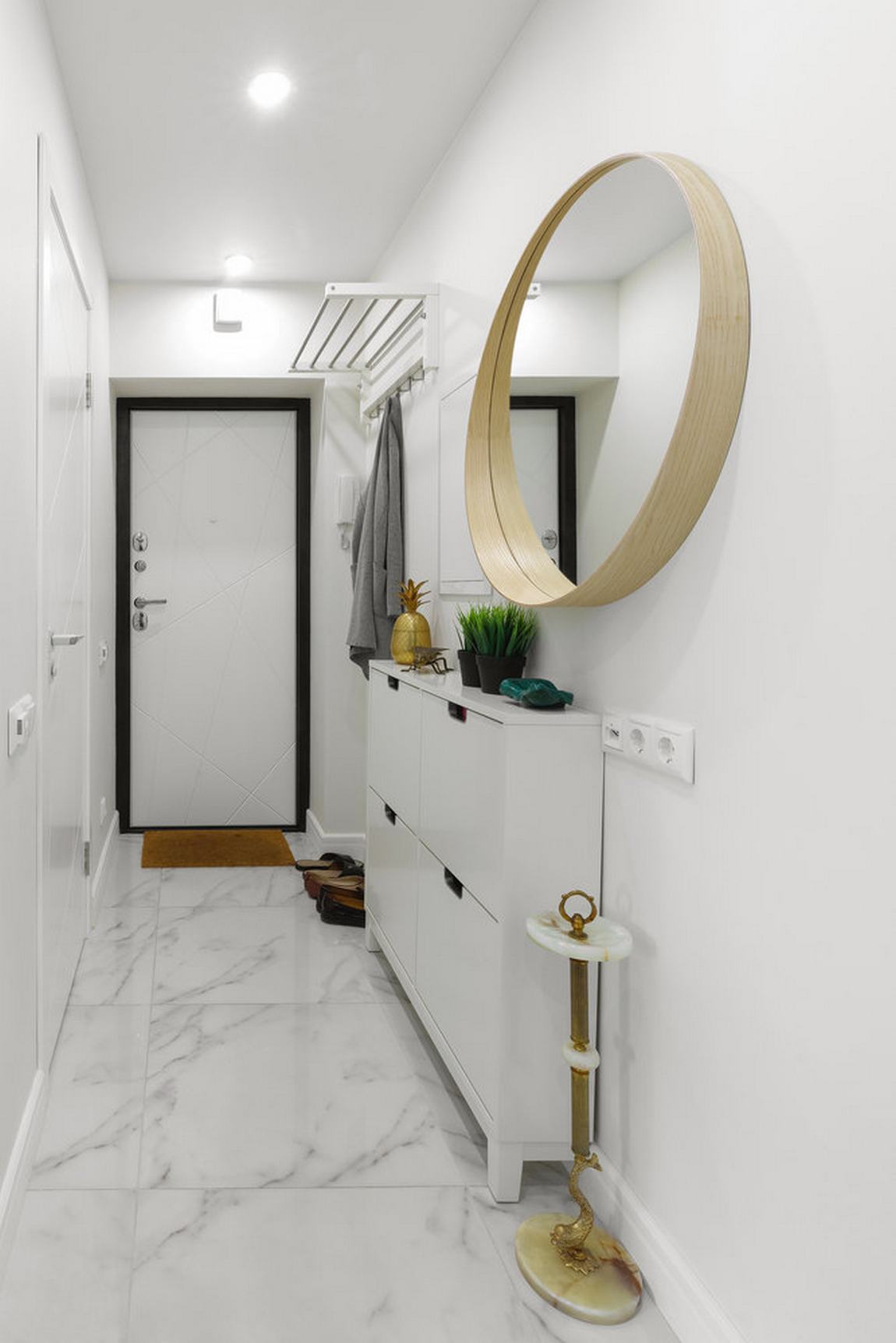 Lối vào căn hộ xinh xắn với tường sơn trắng sạch sẽ, sàn nhà lát đá cẩm thạch sáng bóng, cánh cửa viền khung màu đen tạo điểm nhấn vào chiều sâu cho lối vào nhỏ hẹp.