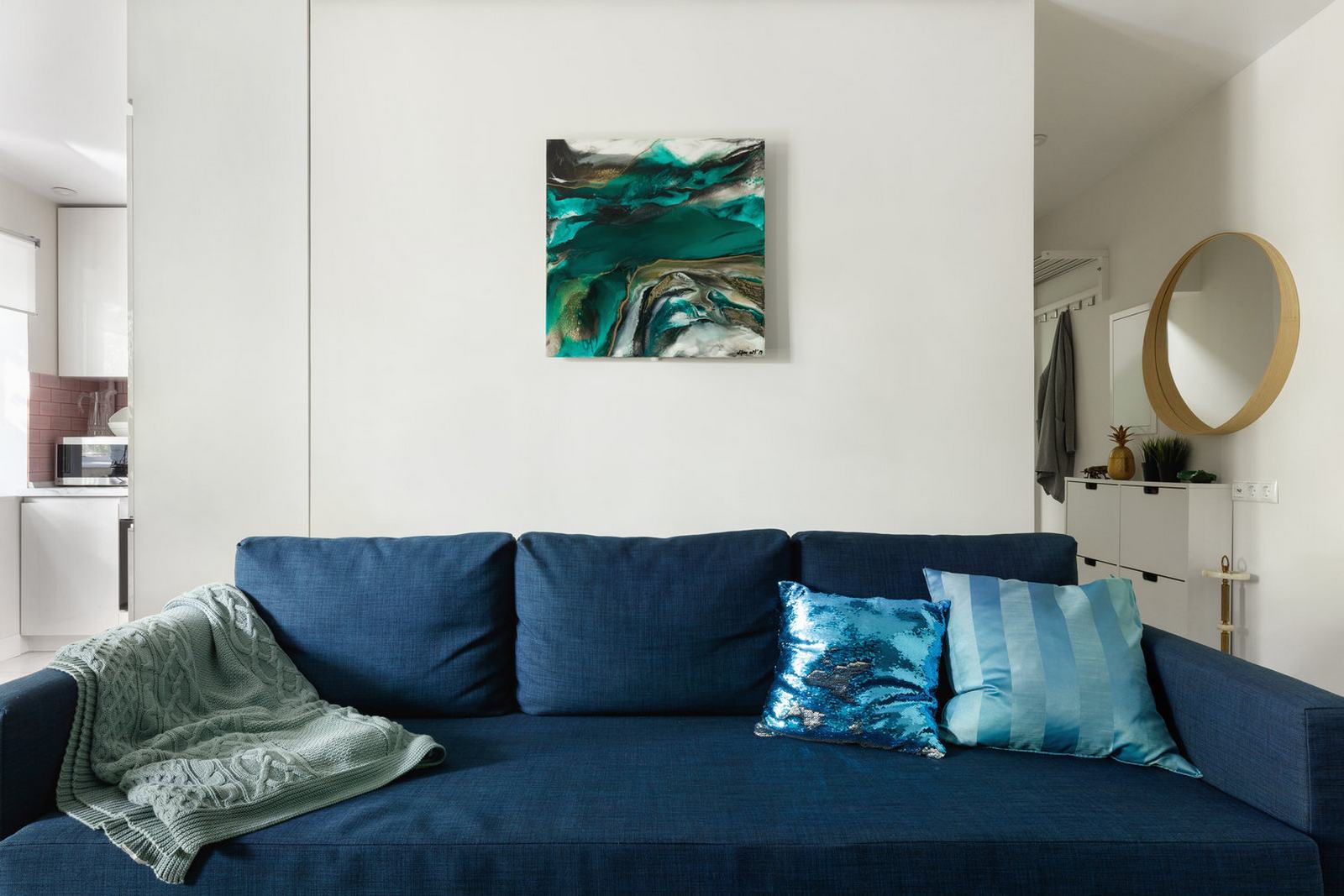 Bức tường đằng sau ghế sofa được trang trí bởi bức tranh trừu tượng, với gam màu pha trộn giữa xanh lam và xanh ngọc lục bảo để tạo sự liên kết bằng thị giác ấn tượng.