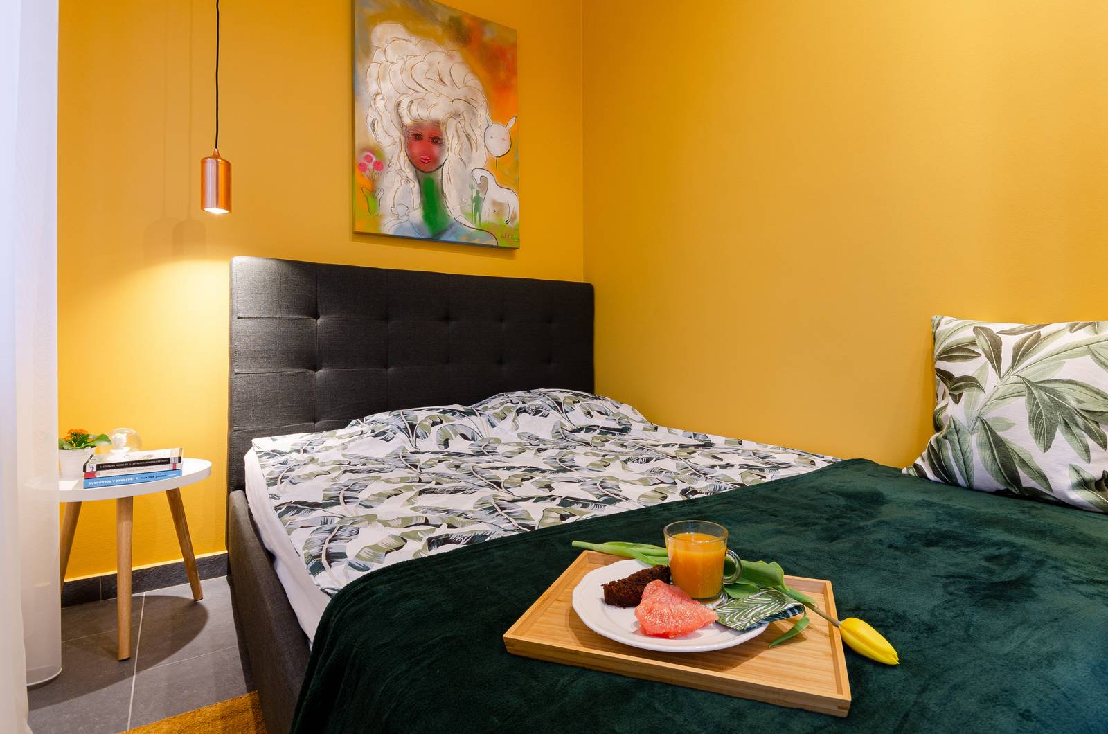 Khung và đầu giường gam màu đen mạnh mẽ, sơn tường vàng mù tạt kết hợp chăn đắp xanh ngọc lục bảo tạo sự kết nối nhất định về màu sắc với nội thất phòng khách.