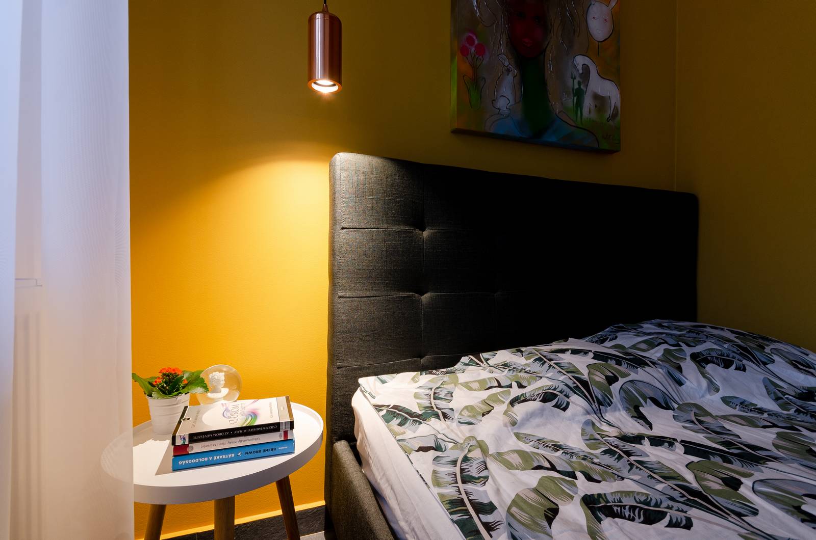 Tấm chăn mỏng hoa văn lá chuối, ánh sáng ấm áp từ đèn thả trần, phụ kiện trang trí trên táp đầu giường và bức tranh cô gái cho không gian vẻ đẹp rất 'art'.