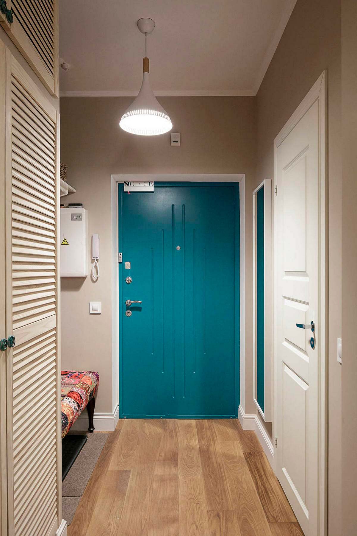 Sảnh vào nhà thu hút với cánh cửa màu xanh lam đậm nổi bật giữa sơn tường màu be đậm và sàn gỗ ấm áp. Chiếc đèn trần chiếu sáng nhẹ nhàng tạo sự gần gũi từ cái nhìn đầu tiên.