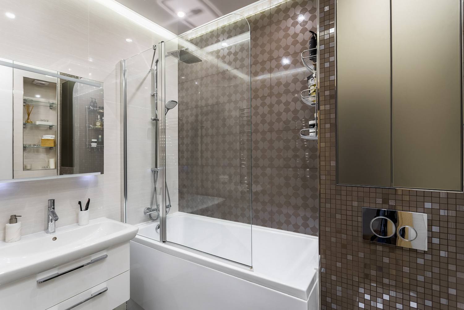 Bước vào khu vực phòng tắm, chúng ta sẽ nhận thấy sự thay đổi màu sắc tương phản giữa trắng và nâu đậm với gạch ốp tường ở khu vực bồn tắm nằm khá bắt mắt, phân vùng với toilet bằng cửa kính trong suốt.
